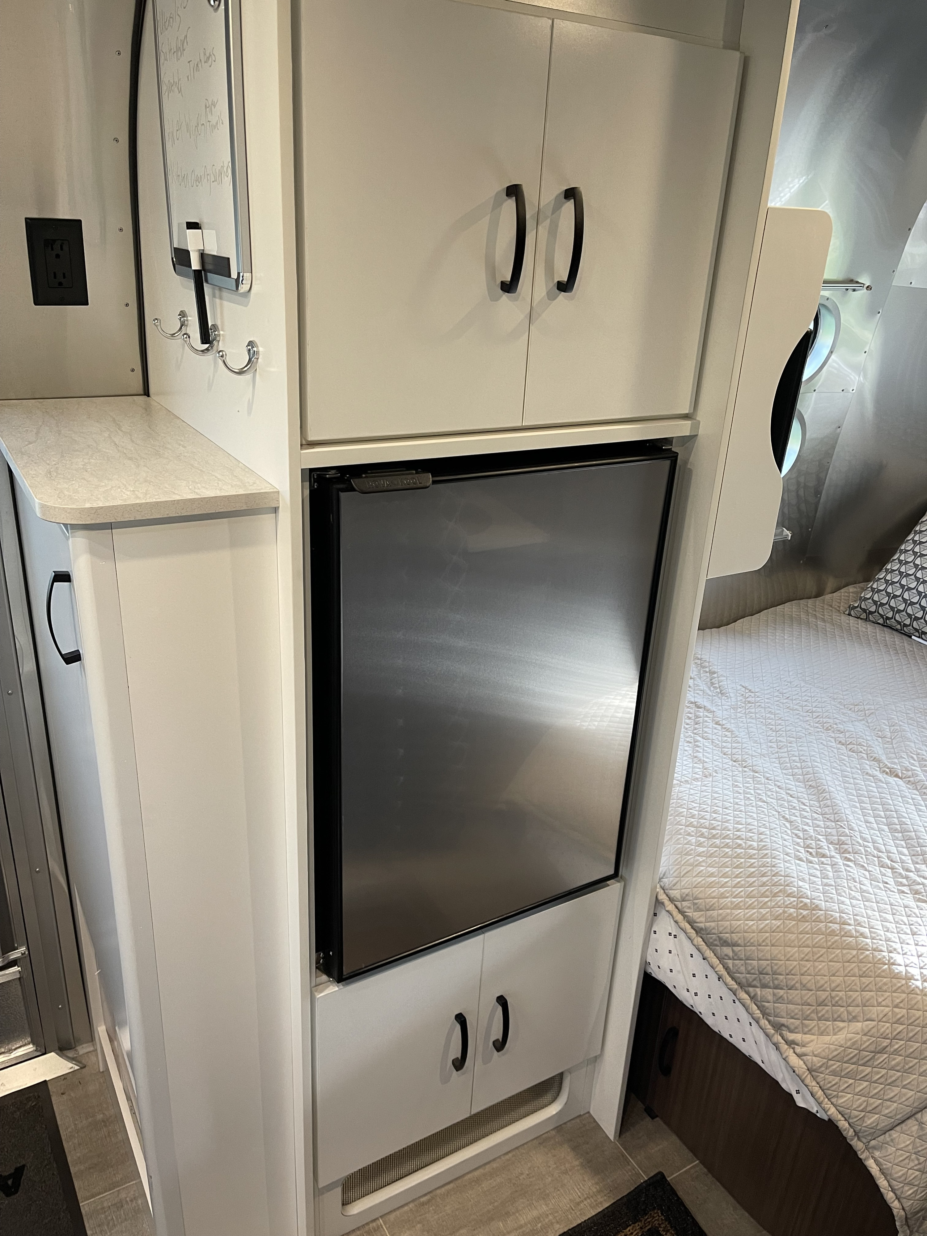 RV rental interior showcasing a compact stainless steel refrigerator, white cabinets, and a cozy bed area.. Airstream Caraval 2021