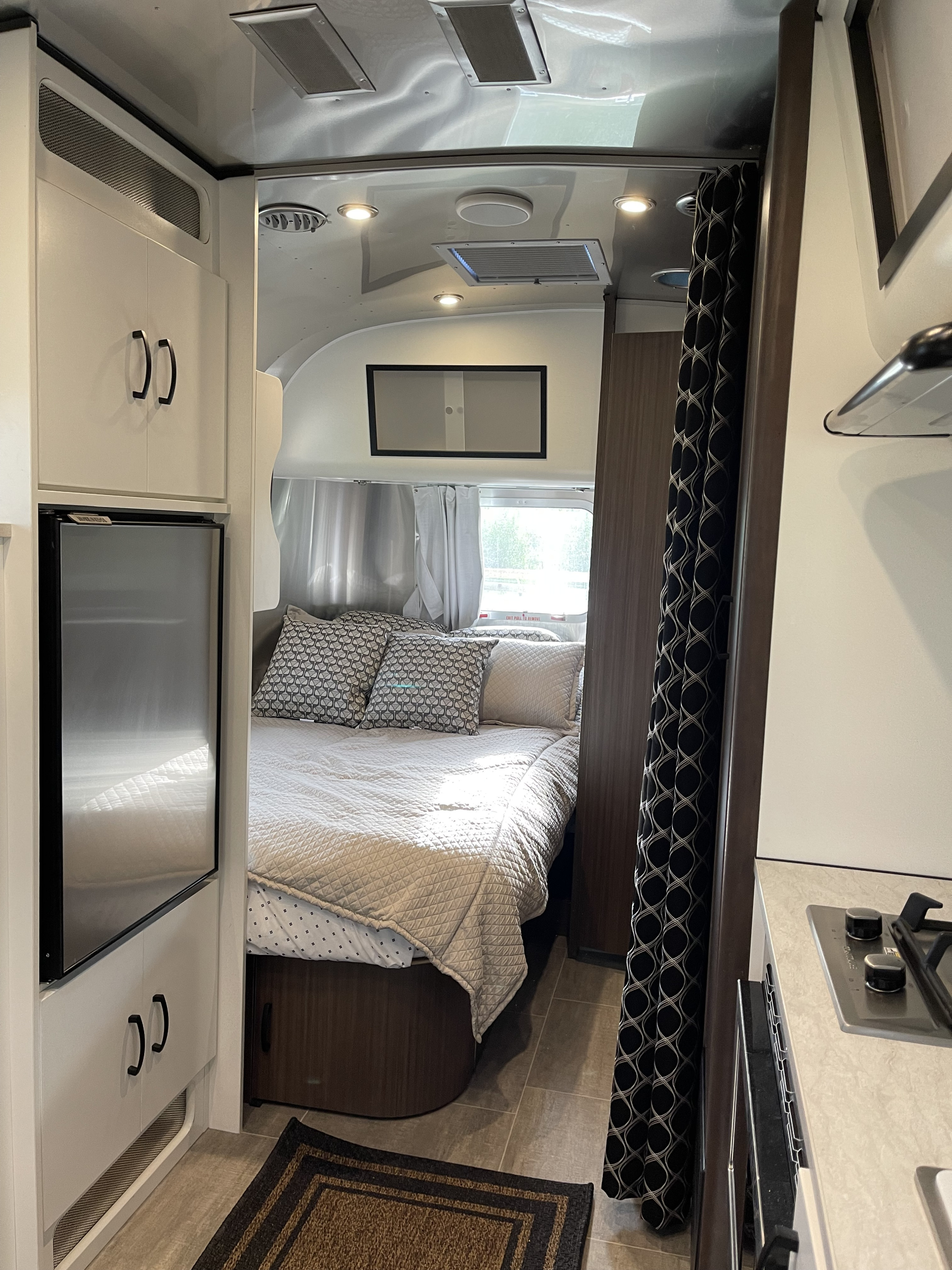 Cozy rv rental interior, showing a neat bedroom with patterned pillows, a shiny ceiling, and a compact kitchen with a stovetop.. Airstream Caraval 2021