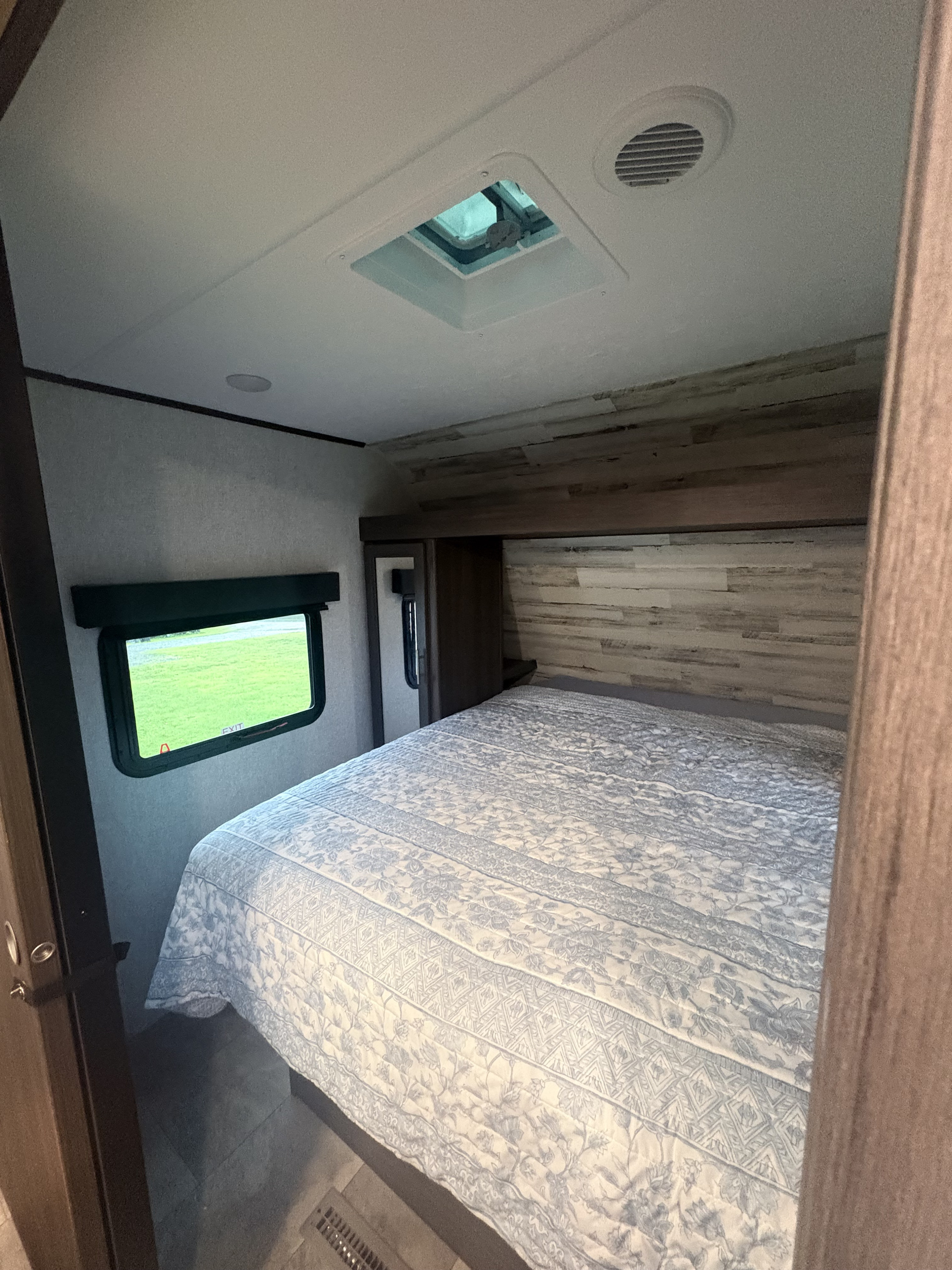 Cozy bedroom in an RV rental, featuring a bed, window with green view, skylight, and rustic wood accent wall.. Dutchmen Kodiak SE 2021