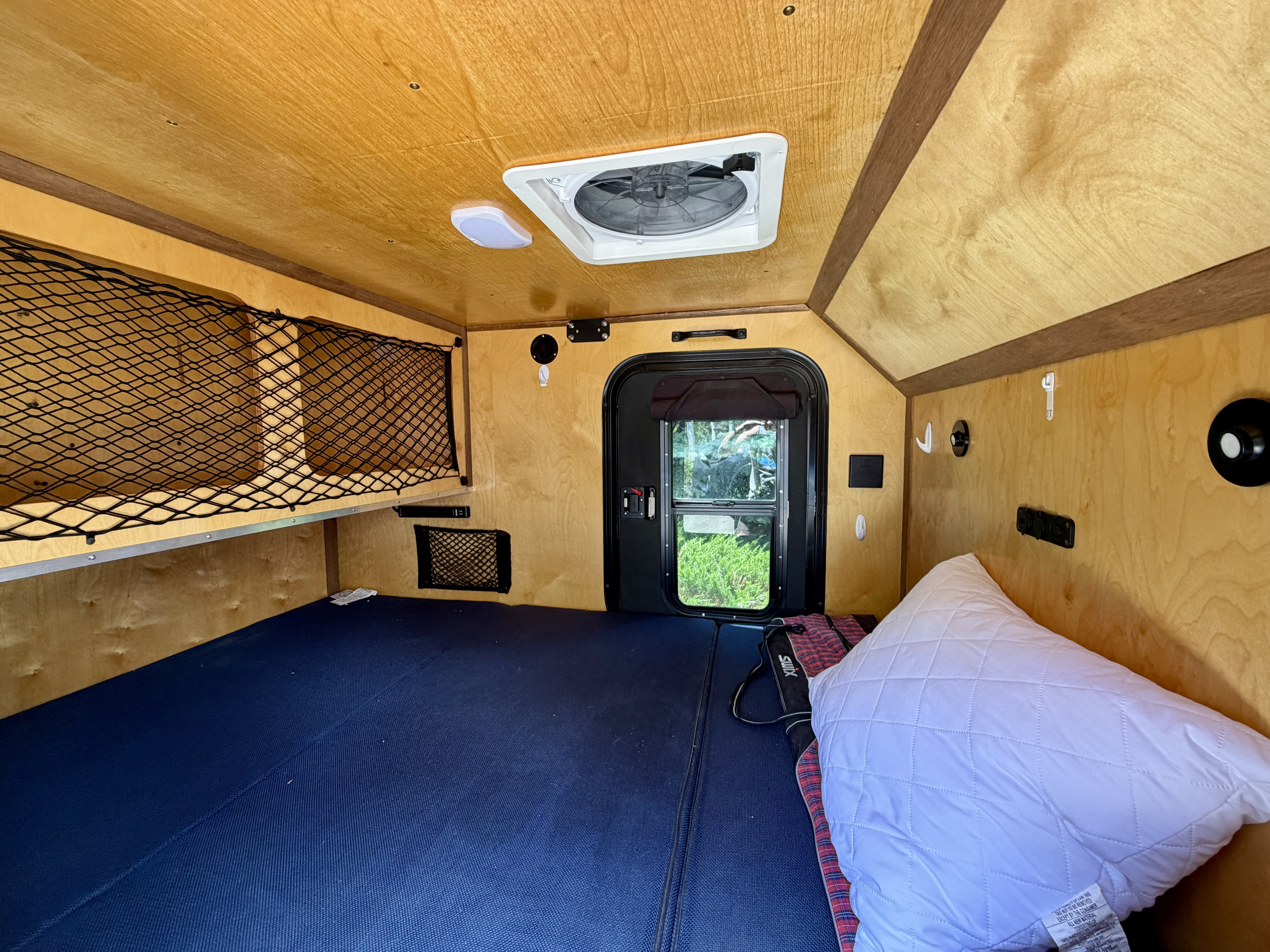 Compact RV rental interior with wooden walls, blue bed, ceiling fan, and storage nets, ready for your next adventure.. Venture Overland Campers XTR 2022