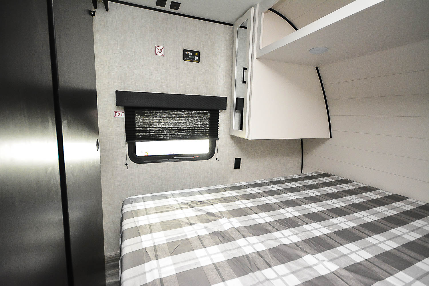 Modern RV rental bedroom: Features a cozy plaid bed, window with blind, overhead storage, and integrated closet for compact living.. Jayco Jay Flight SLX 2025
