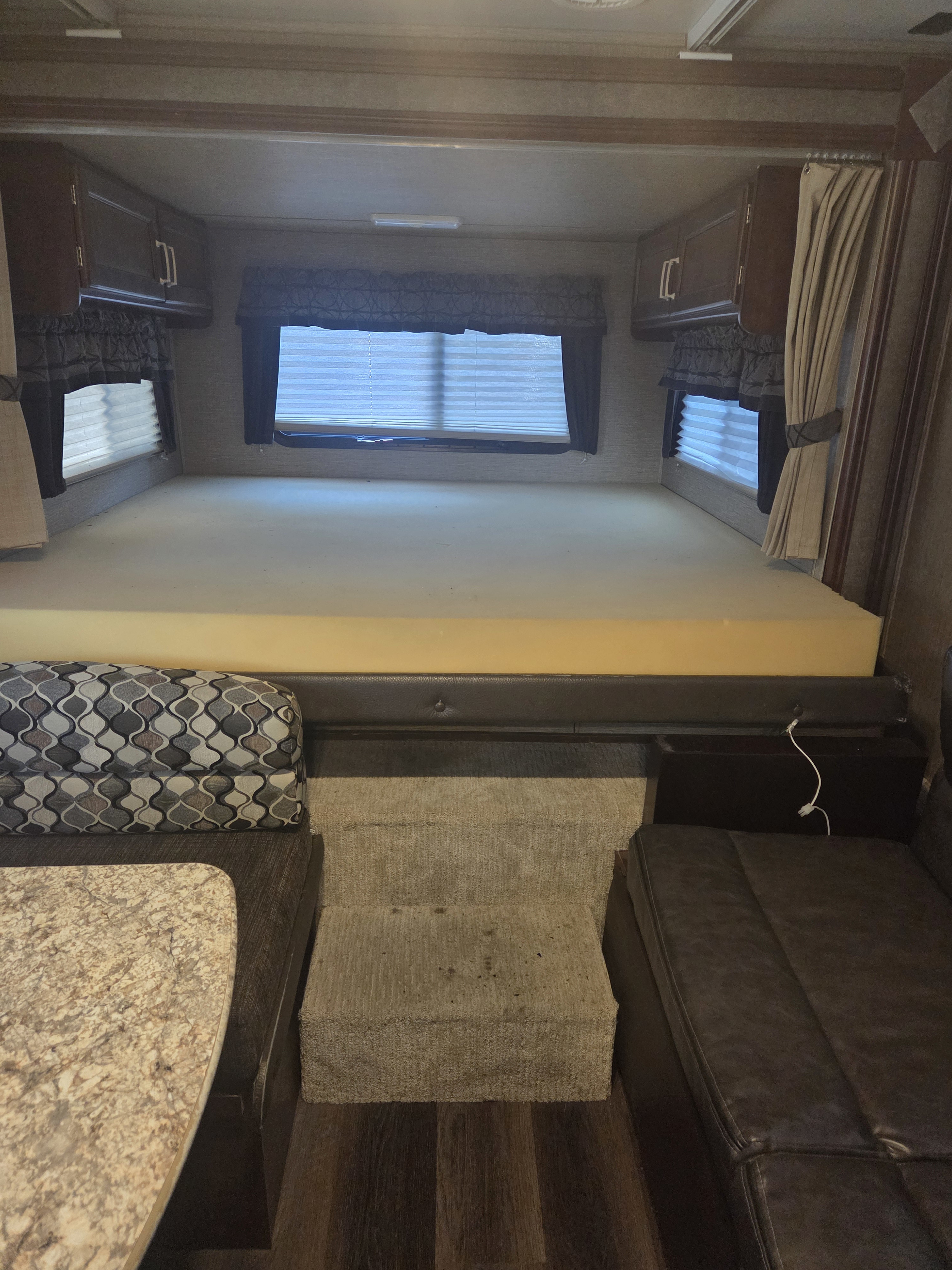 RV rental interior: elevated sleeping area with foam mattress & overhead cabinets, windows, and steps leading to dinette seating.. Keystone Outback 2017