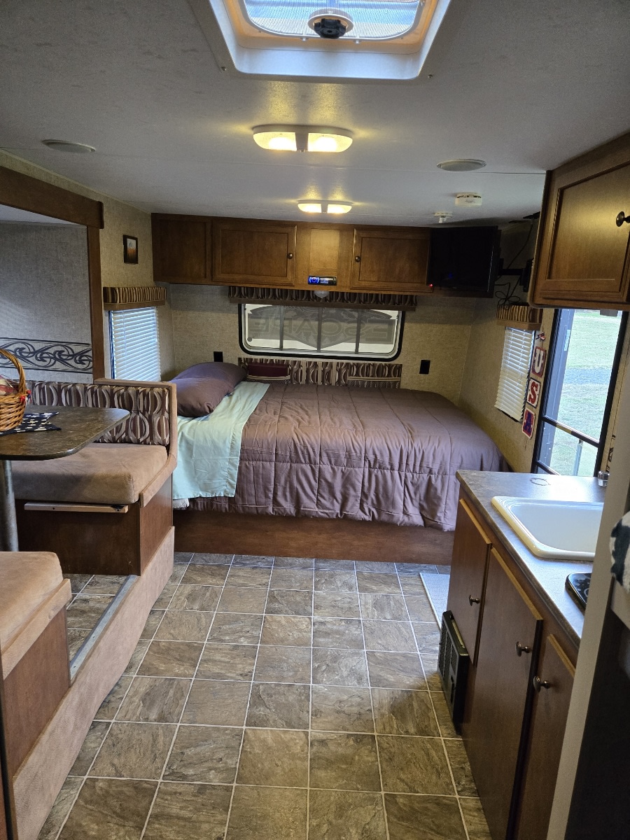 An inviting RV rental interior featuring a bed, dinette, and kitchen area with tiled floors and ample lighting.. Spree Escape 2016