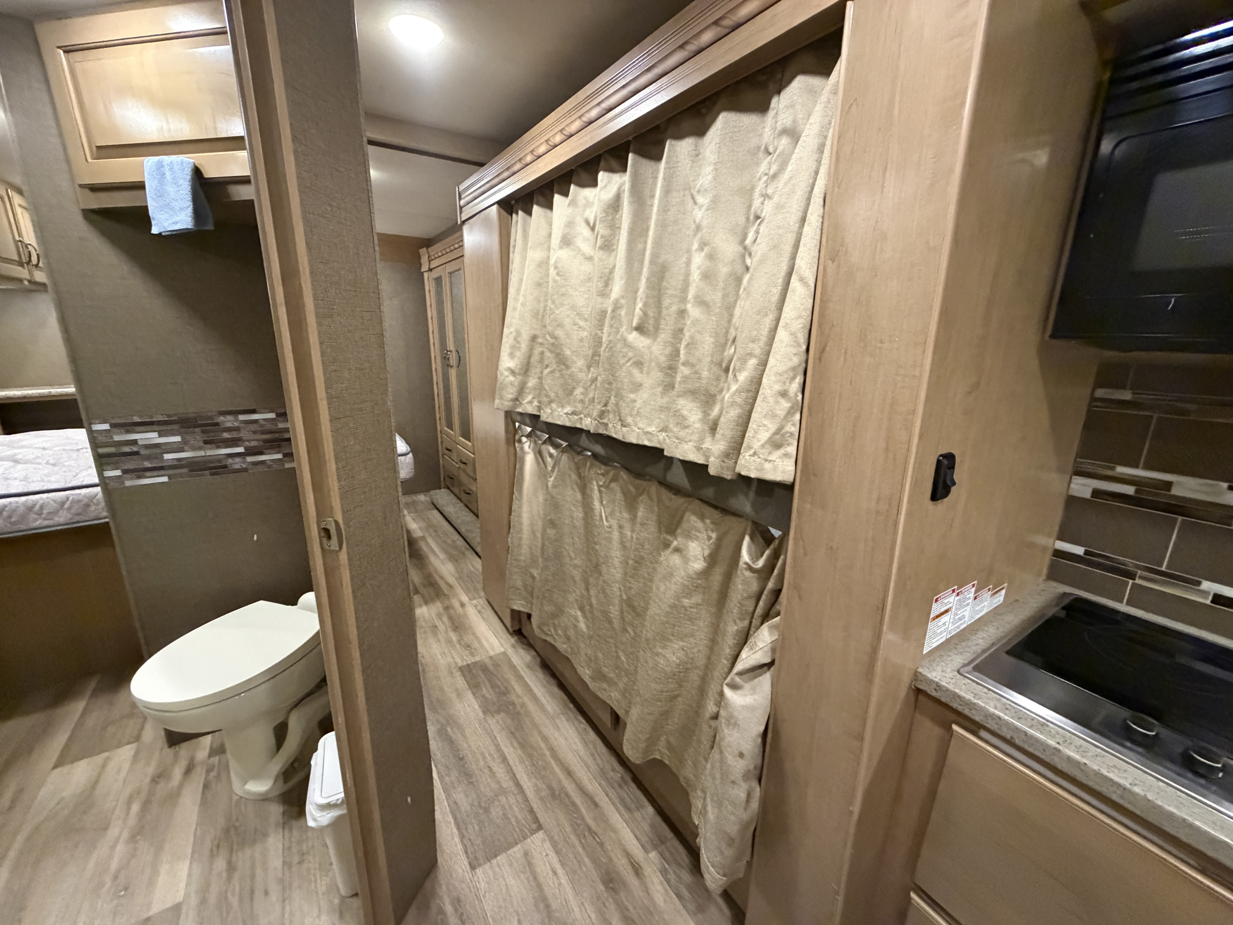 Inside an RV rental: Compact living space featuring a toilet, bunk beds with privacy curtains, and a kitchen stovetop.. Thor Four Winds 2018