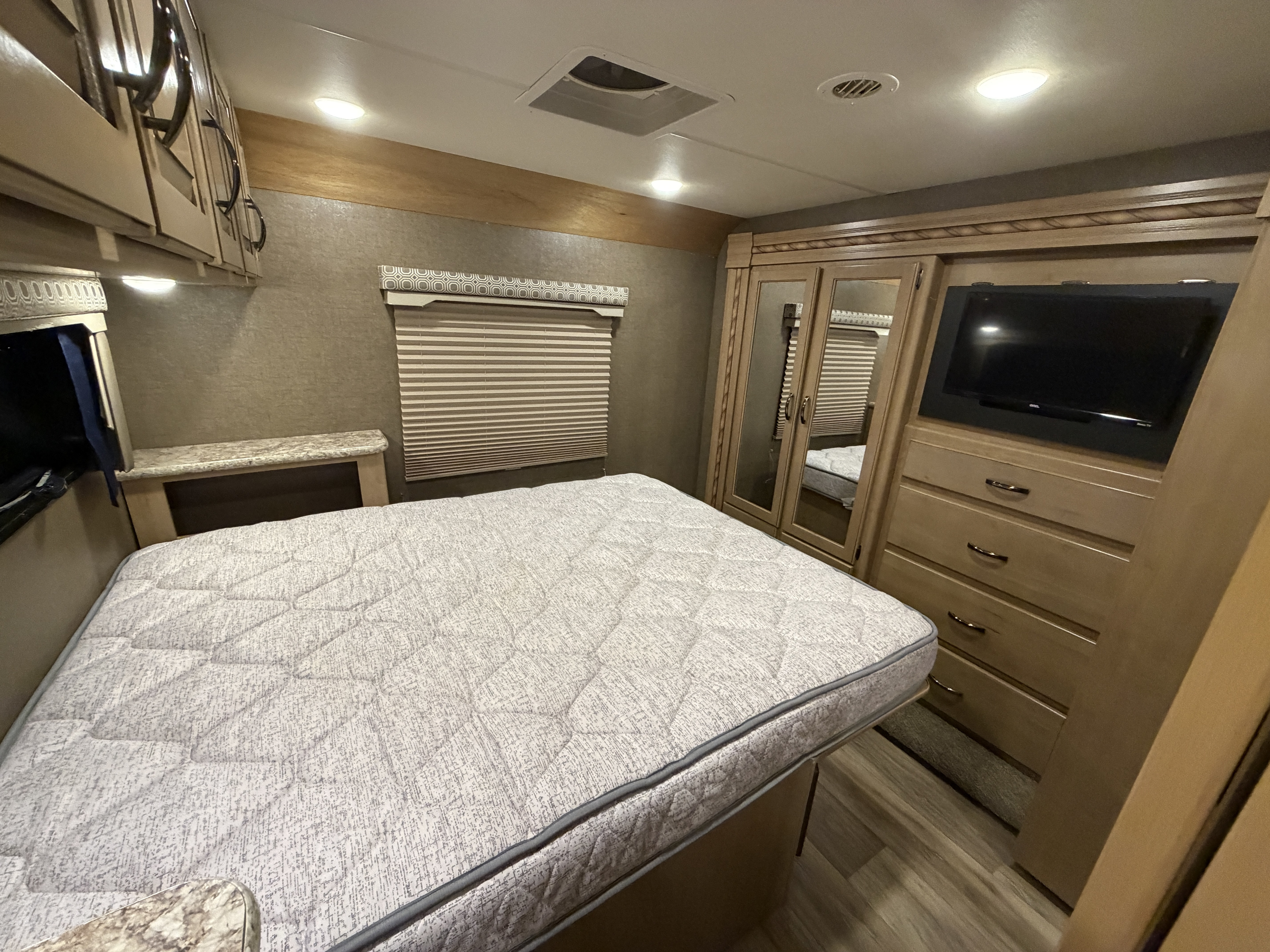 Spacious RV rental bedroom with a comfortable bed, built-in storage including a wardrobe and dresser, and a mounted TV.. Thor Four Winds 2018