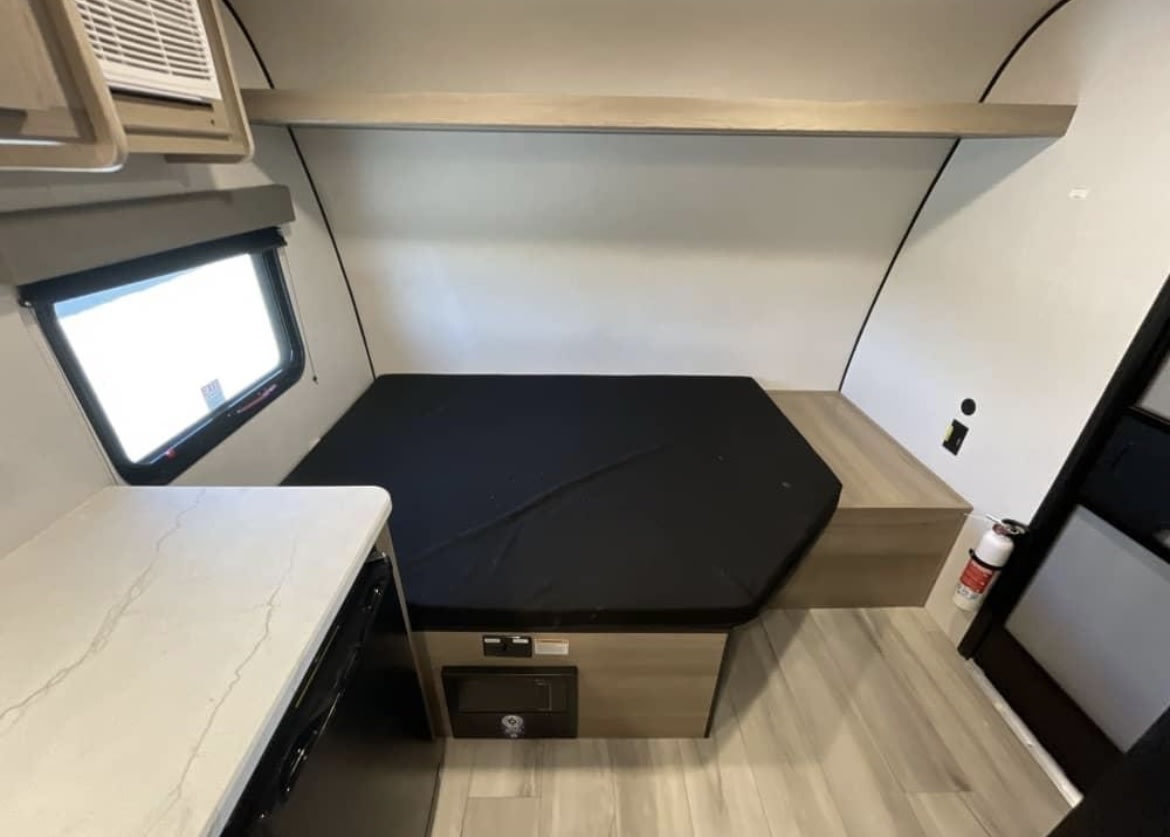 Compact rv rental interior with a hexagonal bed, small counter, window, and fire extinguisher for safety.. 4YDTCME14TM932345 13B 2025