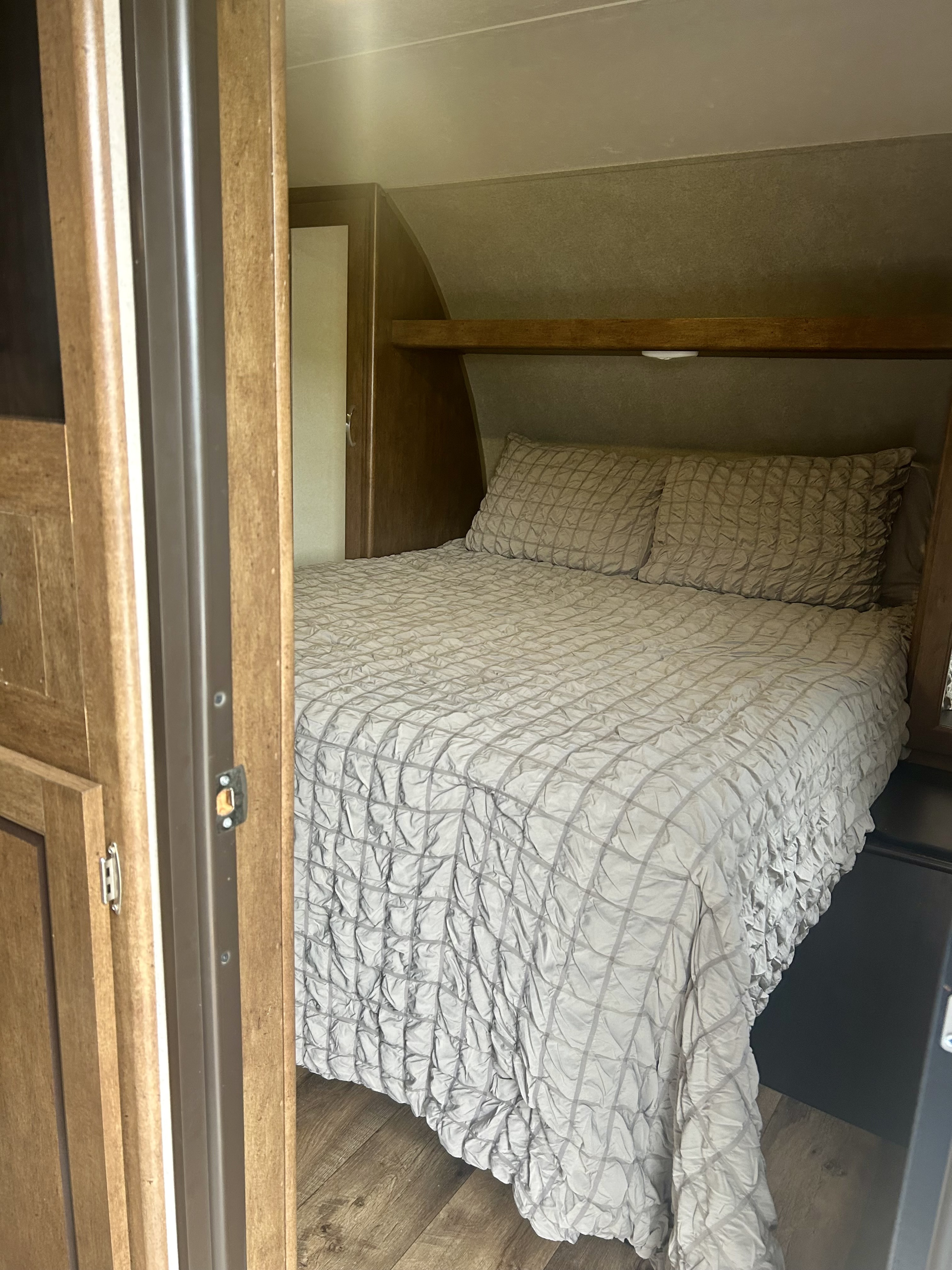 Inside an RV rental: a compact bedroom with a soft, textured bed, pillows, and wooden trim for comfortable travel.. Forest River Salem 2017