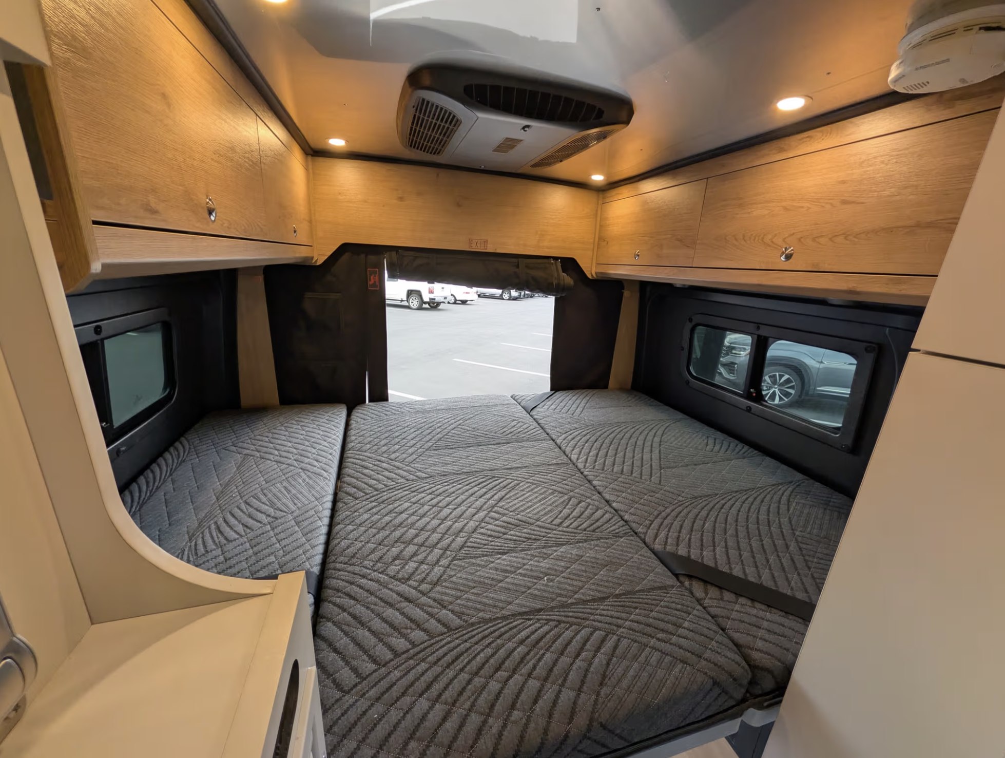RV rental's cozy rear bed area with quilted mattresses, overhead cabinets, and AC, ideal for camper van adventures.. Airstream Rangeline 2024