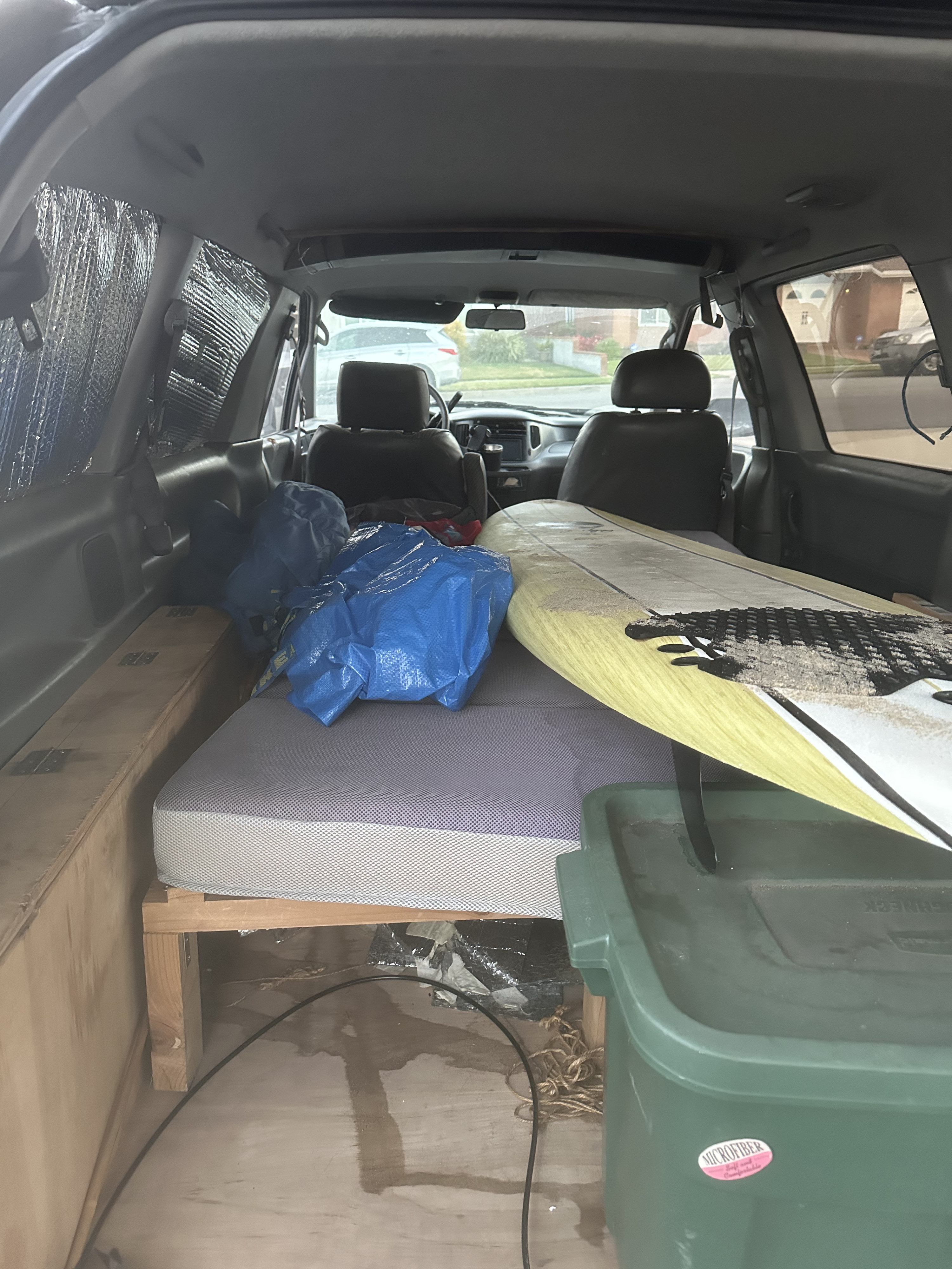 Van interior converted for camping: bed, surfboard, bags, and storage bin. Ready for a road trip or practical rv rental use.. Toyota Previa 1996