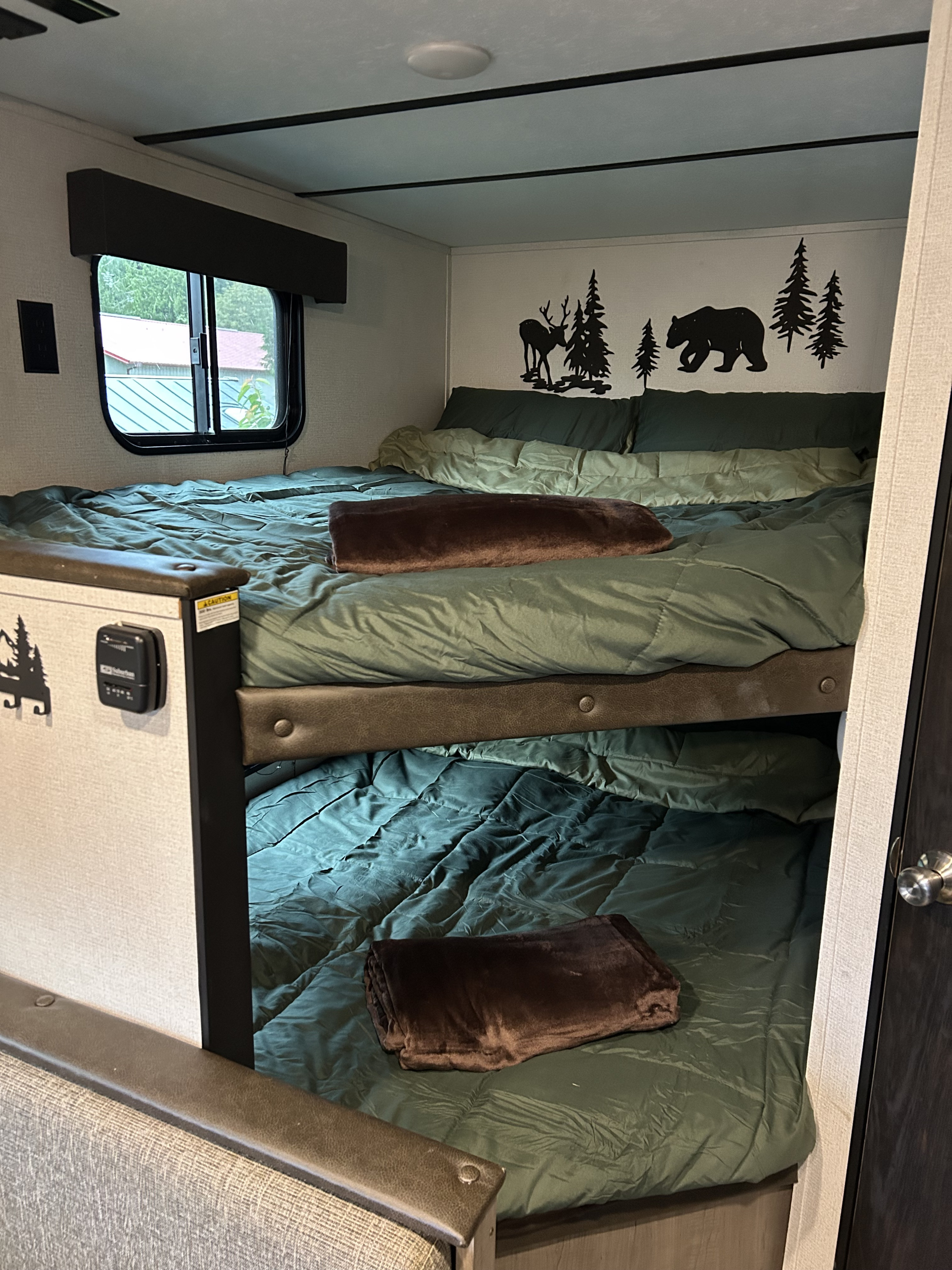 Cozy RV rental bunk beds with green bedding, brown blankets, and nature-themed decals. Perfect for a family camping trip.. Keystone RV Hideout 2021