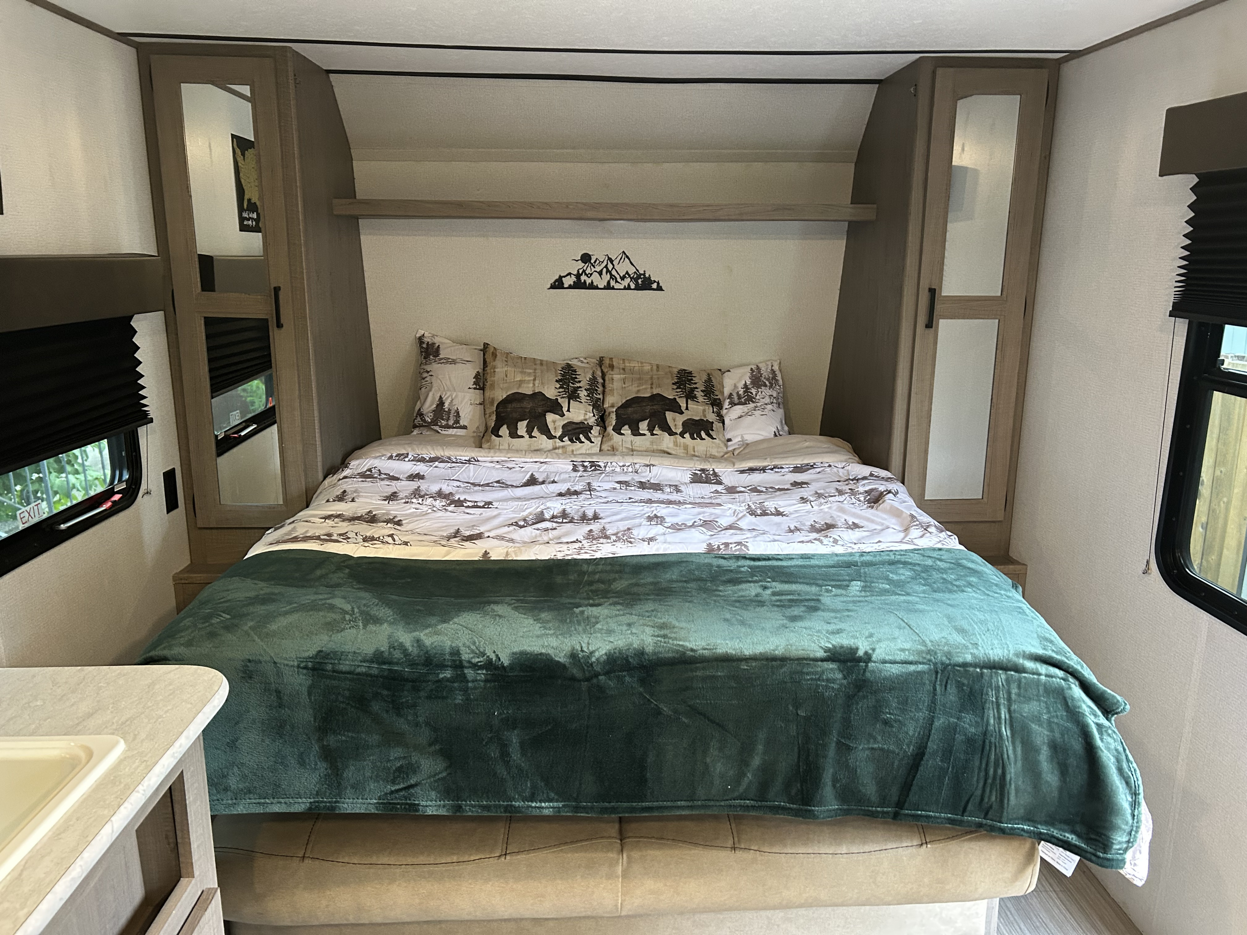 This RV rental features a comfortable bedroom with bear and mountain-themed bedding, storage, and a window.. Keystone RV Hideout 2021