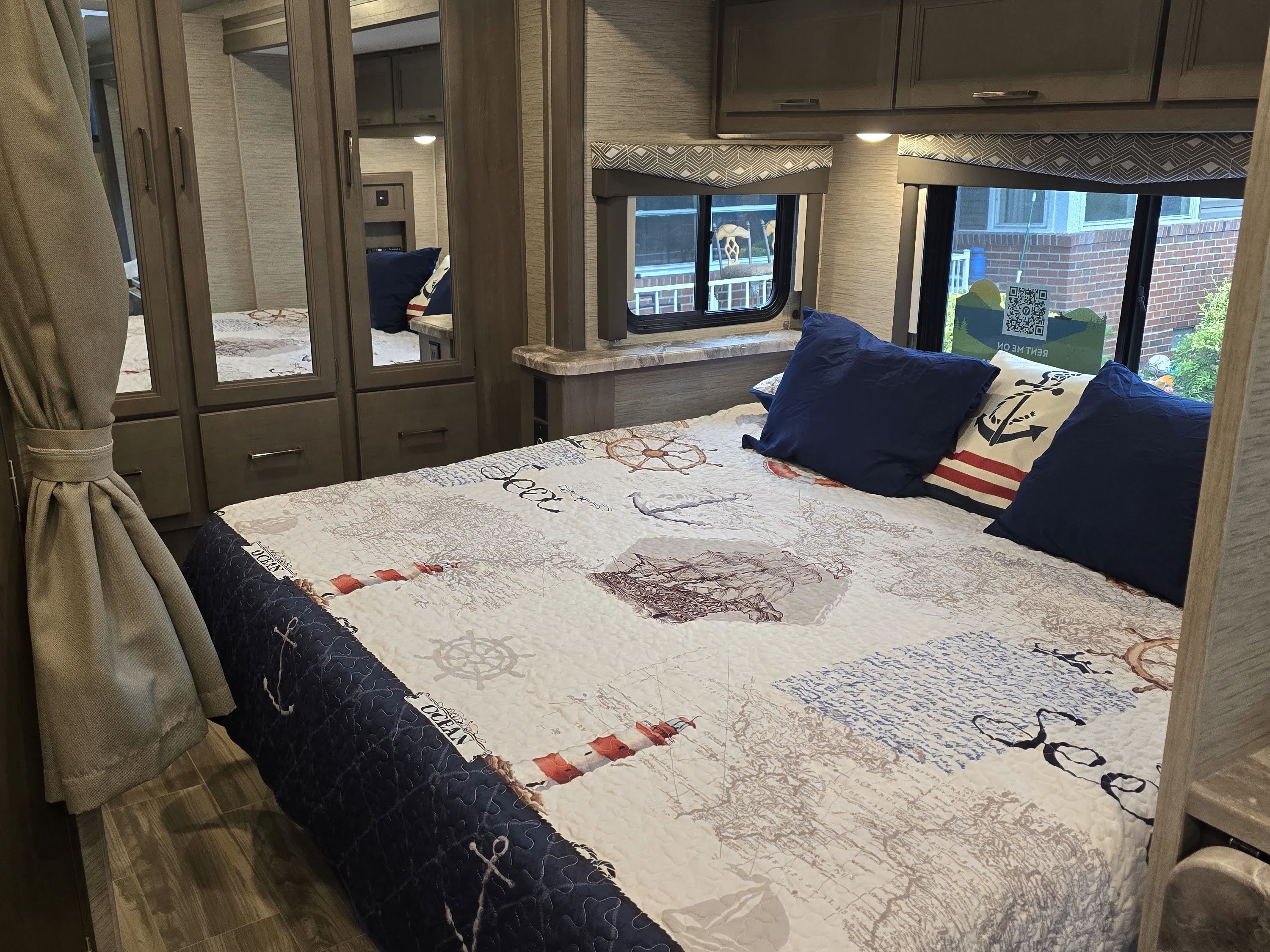 Cozy RV rental bedroom with a nautical-themed quilt, blue pillows, and mirrored closet. Ideal for travel adventures.. Thor Four Winds 2023