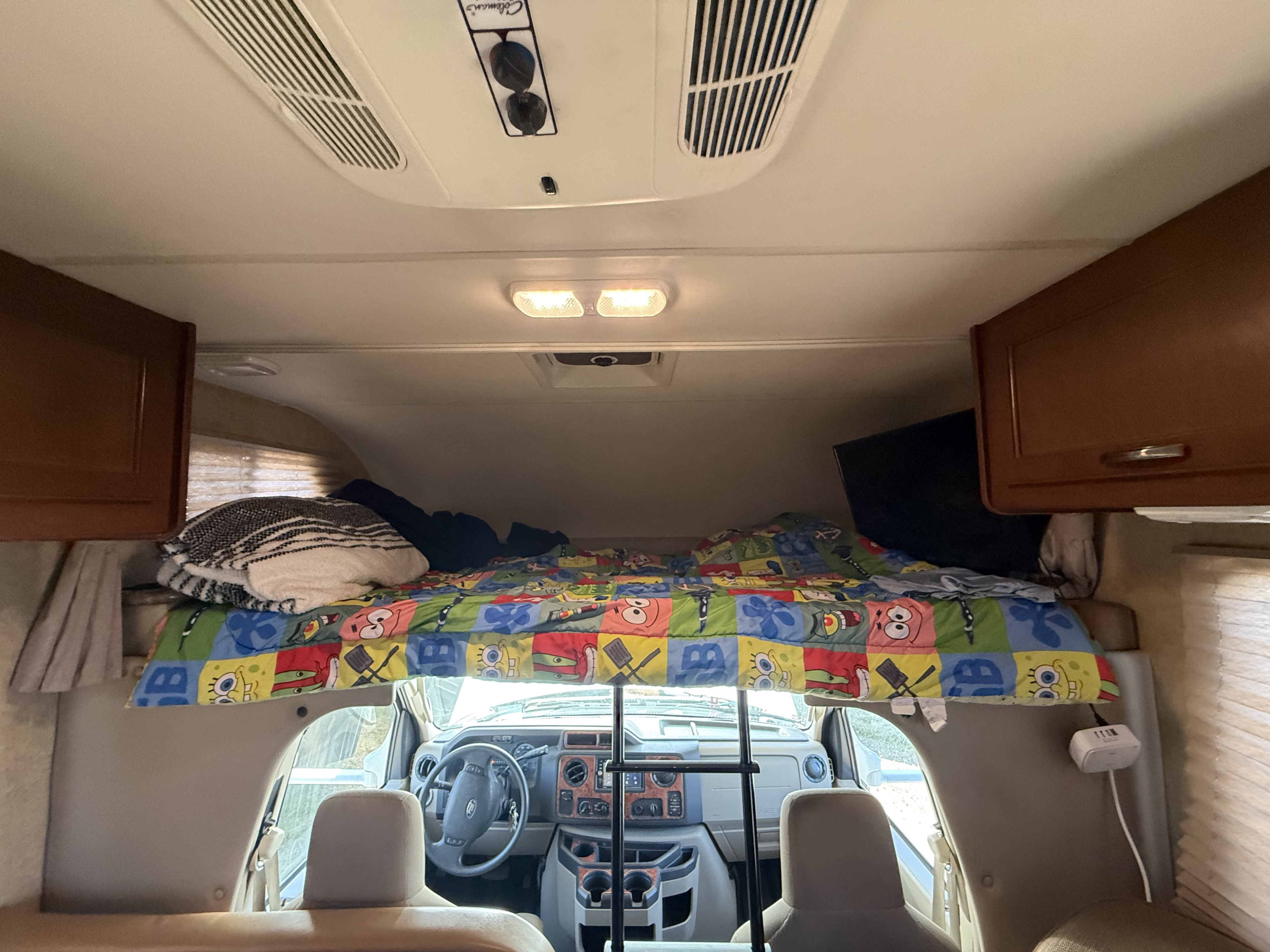 RV rental's overhead bunk with Spongebob comforter and view into the front cab, alongside ceiling AC and storage.. Thor Chateau 2017