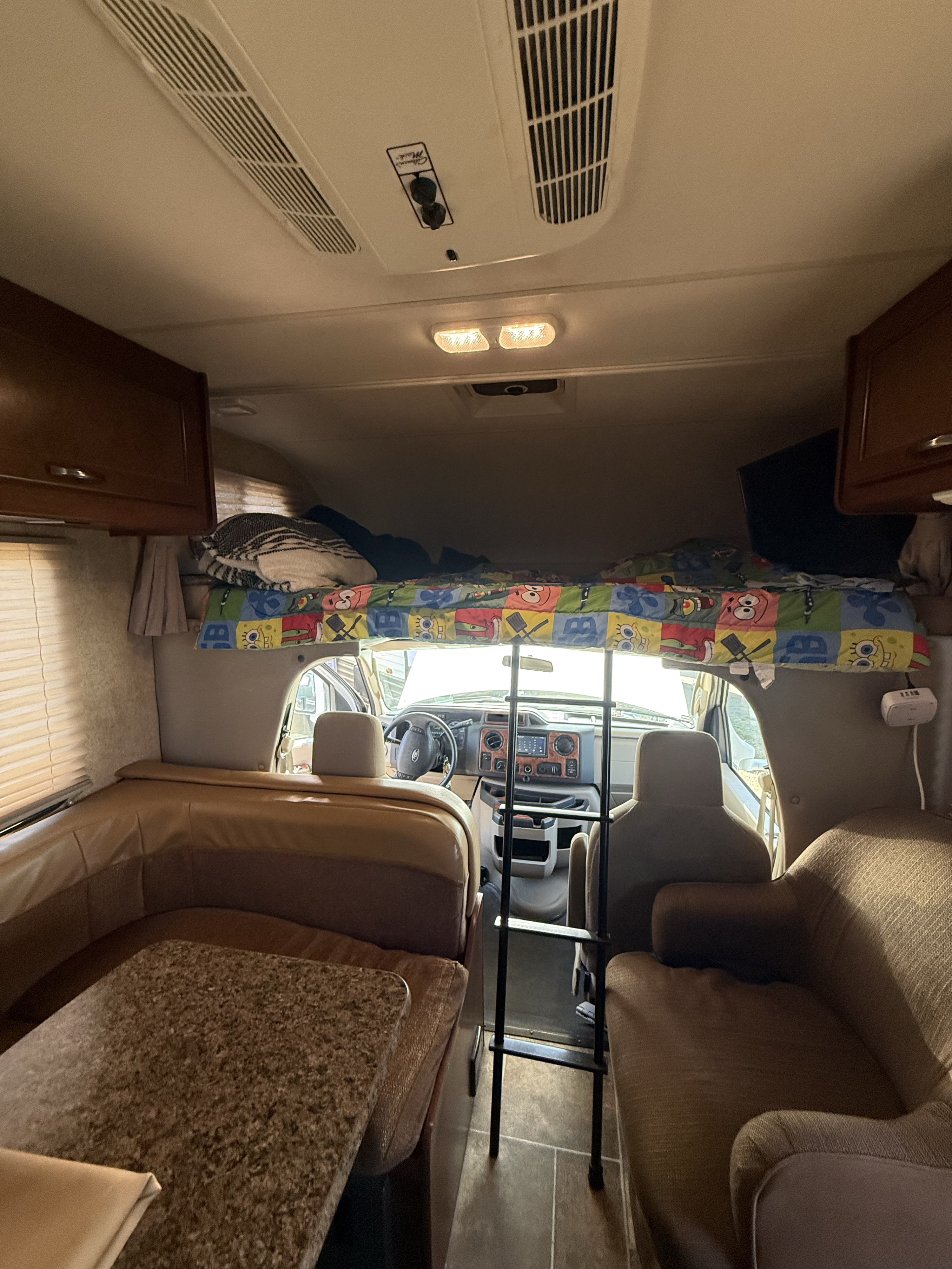 Inside this RV rental: a comfy dining area, an overhead bunk bed with a ladder, and the front driver's cab area.. Thor Chateau 2017