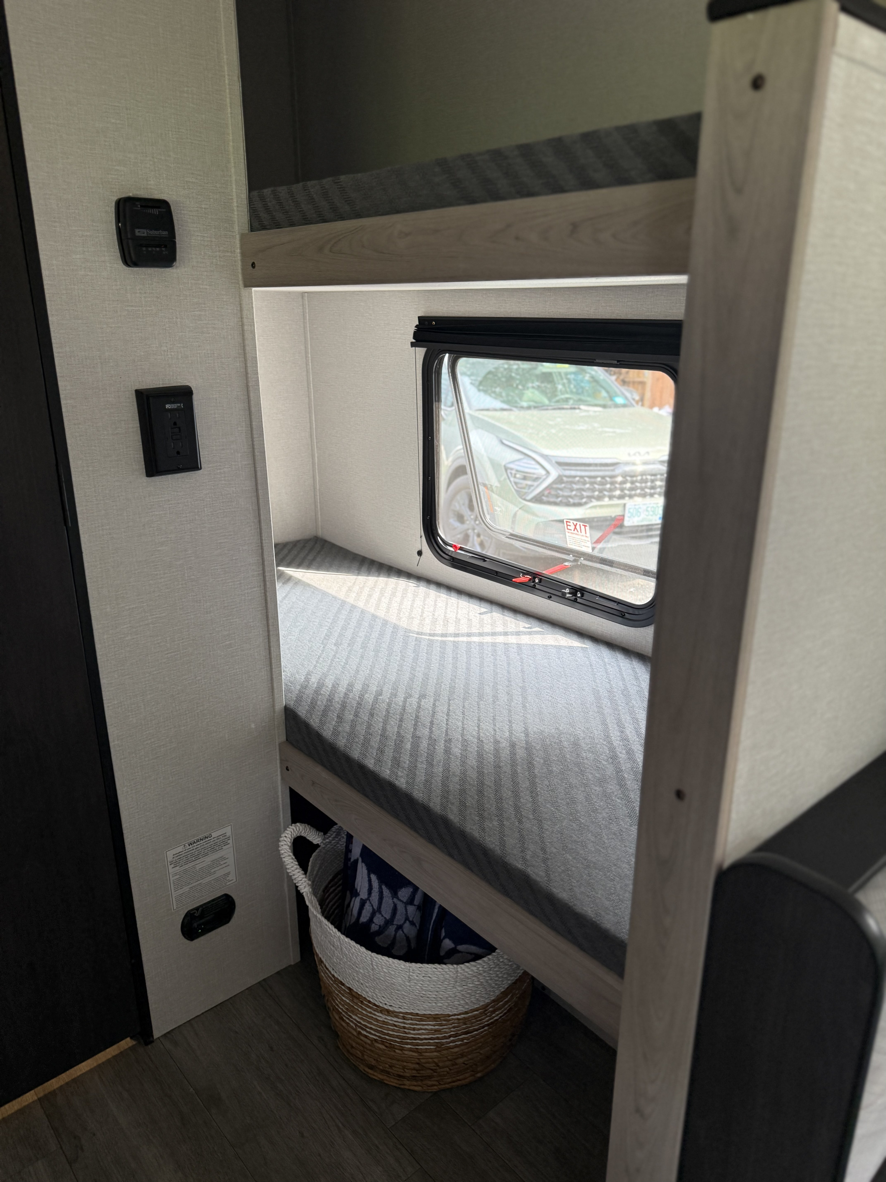 RV rental bunk beds with a window overlooking a car. Features a Suburban thermostat, outlet, and storage basket.. Heartland's RV Mallard 17 BHL 2025