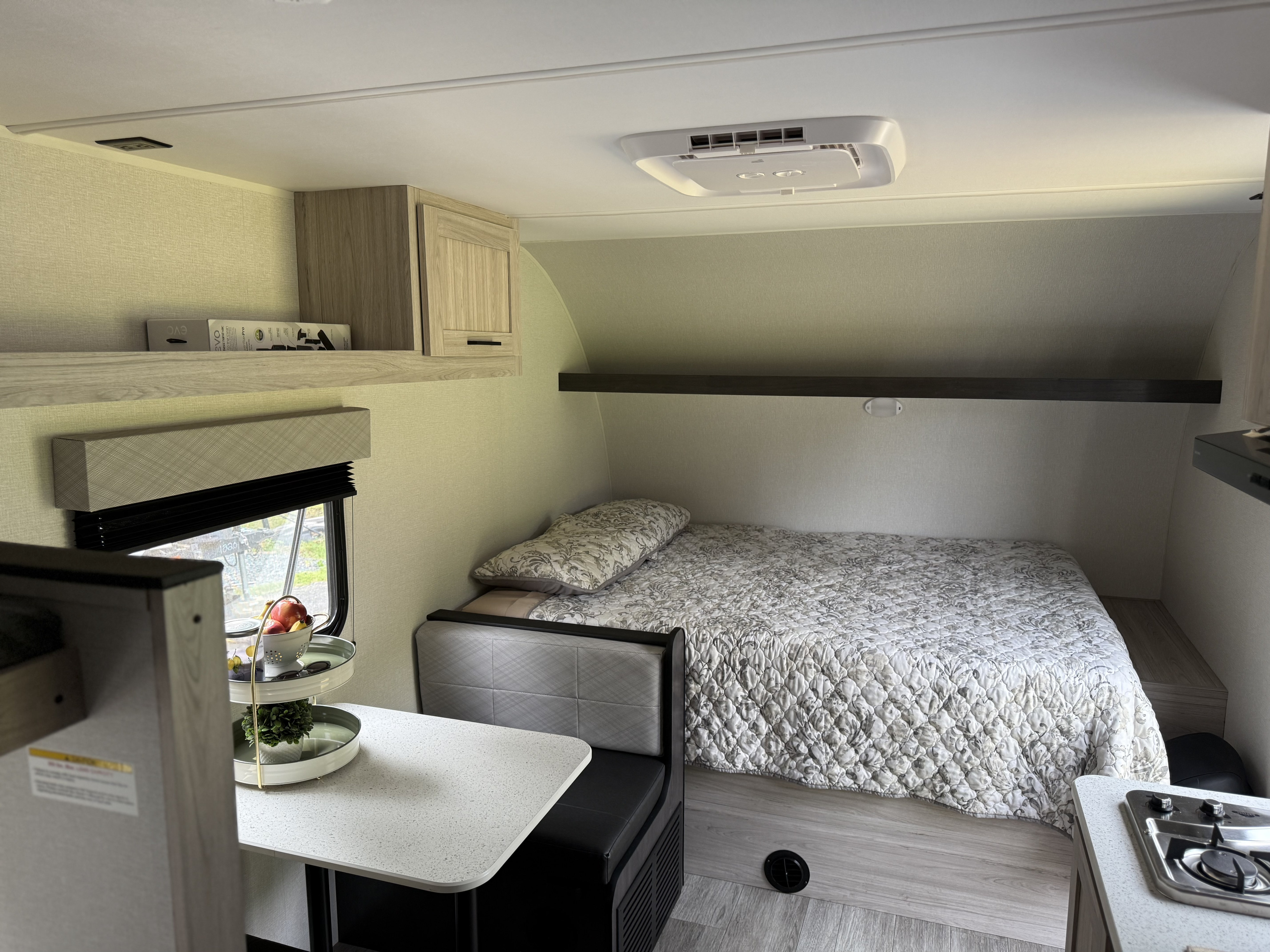 Cozy RV rental interior with bed, dinette, kitchenette, and overhead storage. Features light wood tones and a window view.. Heartland's RV Mallard 17 BHL 2025
