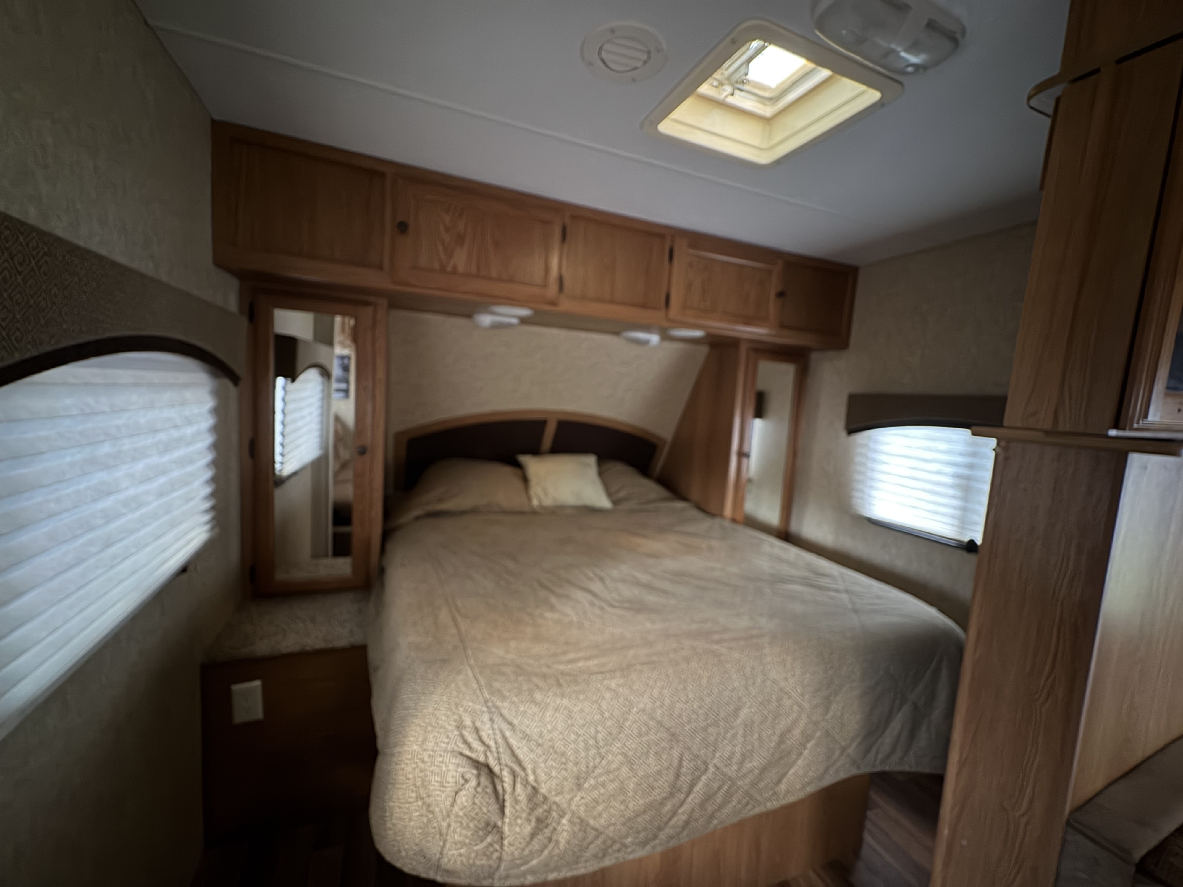 Comfortable RV rental bedroom featuring a queen bed, overhead cabinets, windows with blinds, and a skylight for a cozy stay.. Coachmen Lantern Travel Trailer 2011