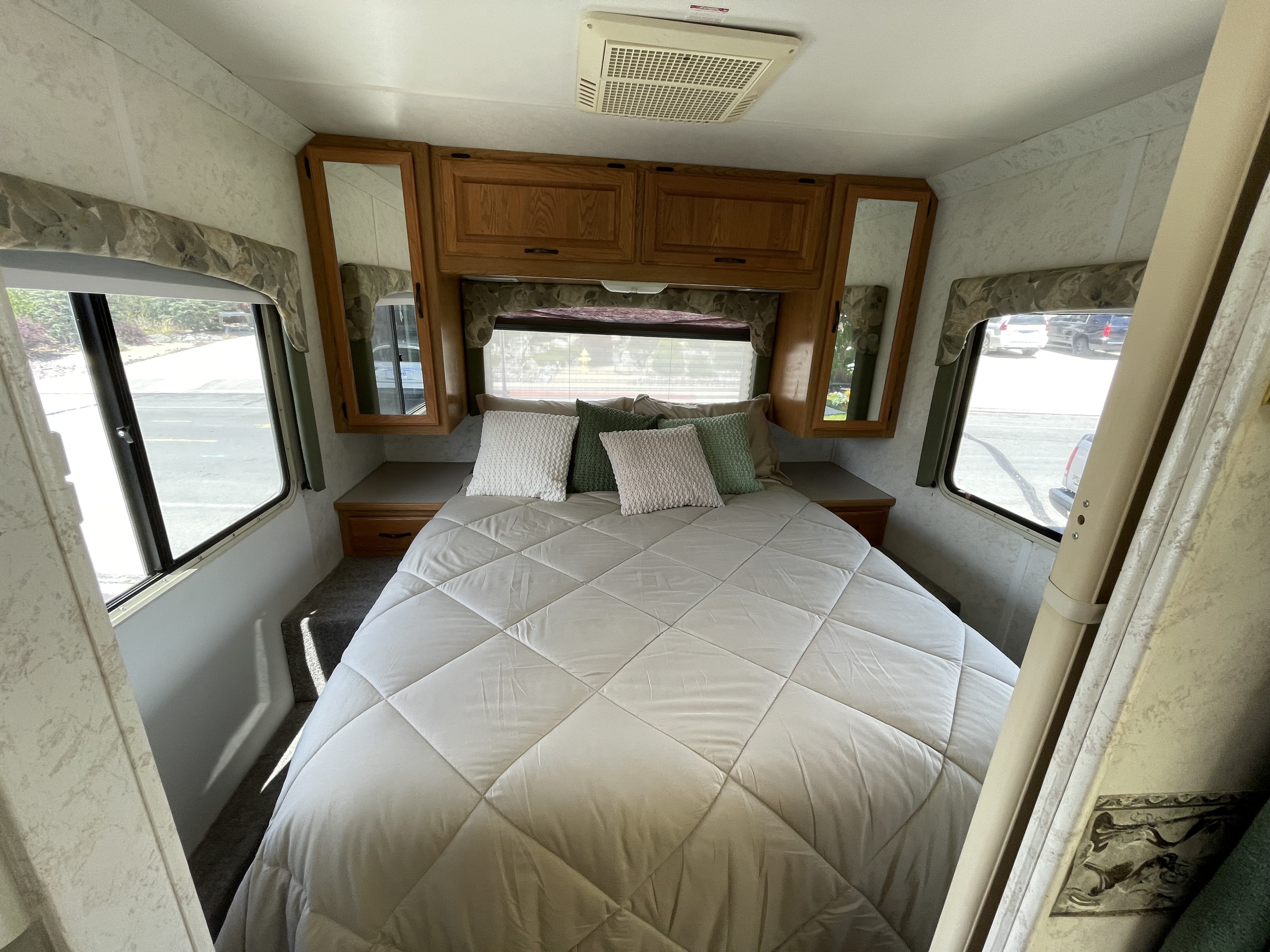 RV rental bedroom displaying a comfortable bed, overhead wooden cabinets with mirrors, windows, and an AC unit.. Four Winds Hurricane 2000