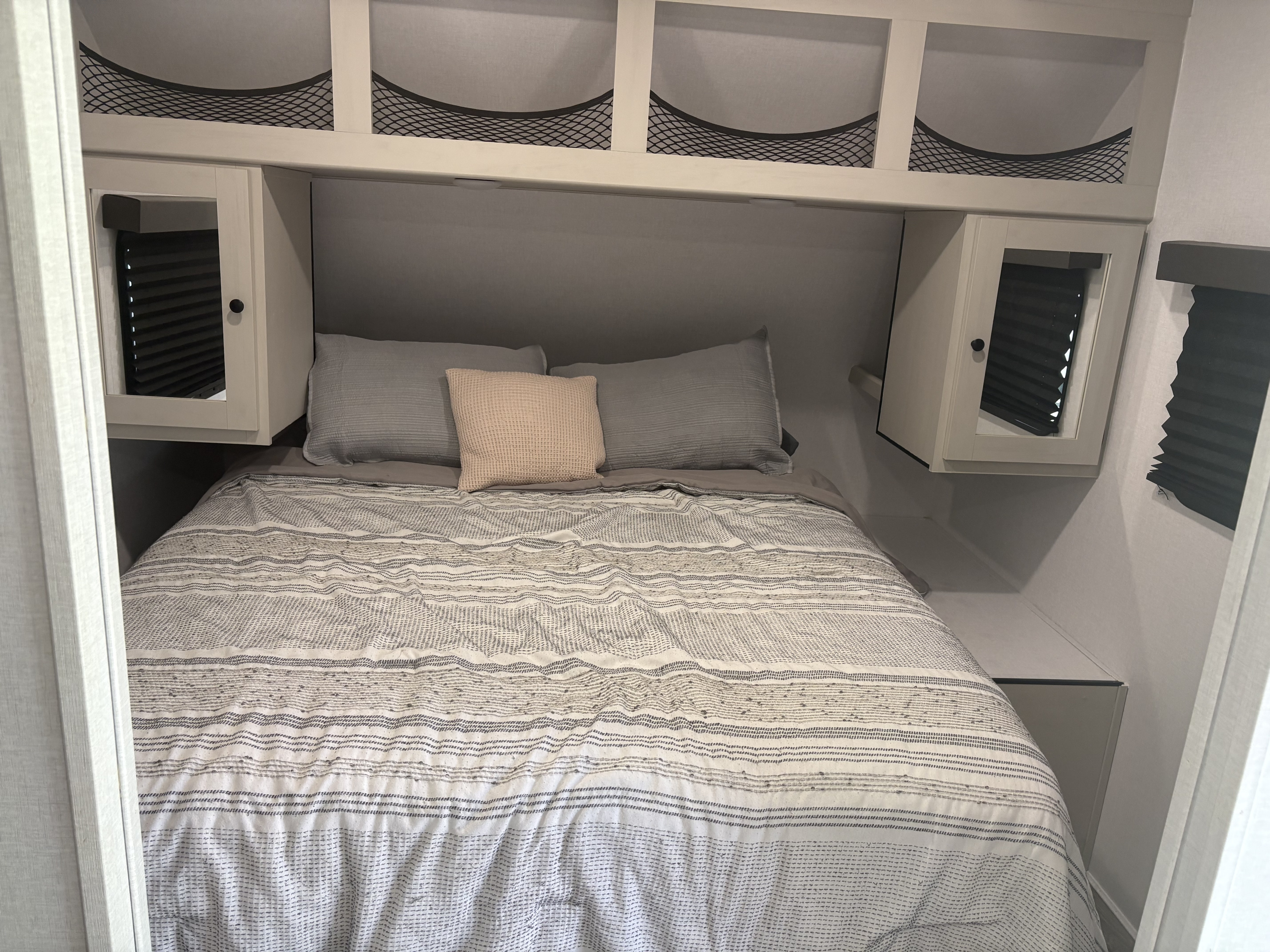 RV rental bedroom: cozy bed with patterned bedding, overhead storage, and mirrored side cabinets in a travel trailer.. Coachmen Northern Spirit 26BH 2025