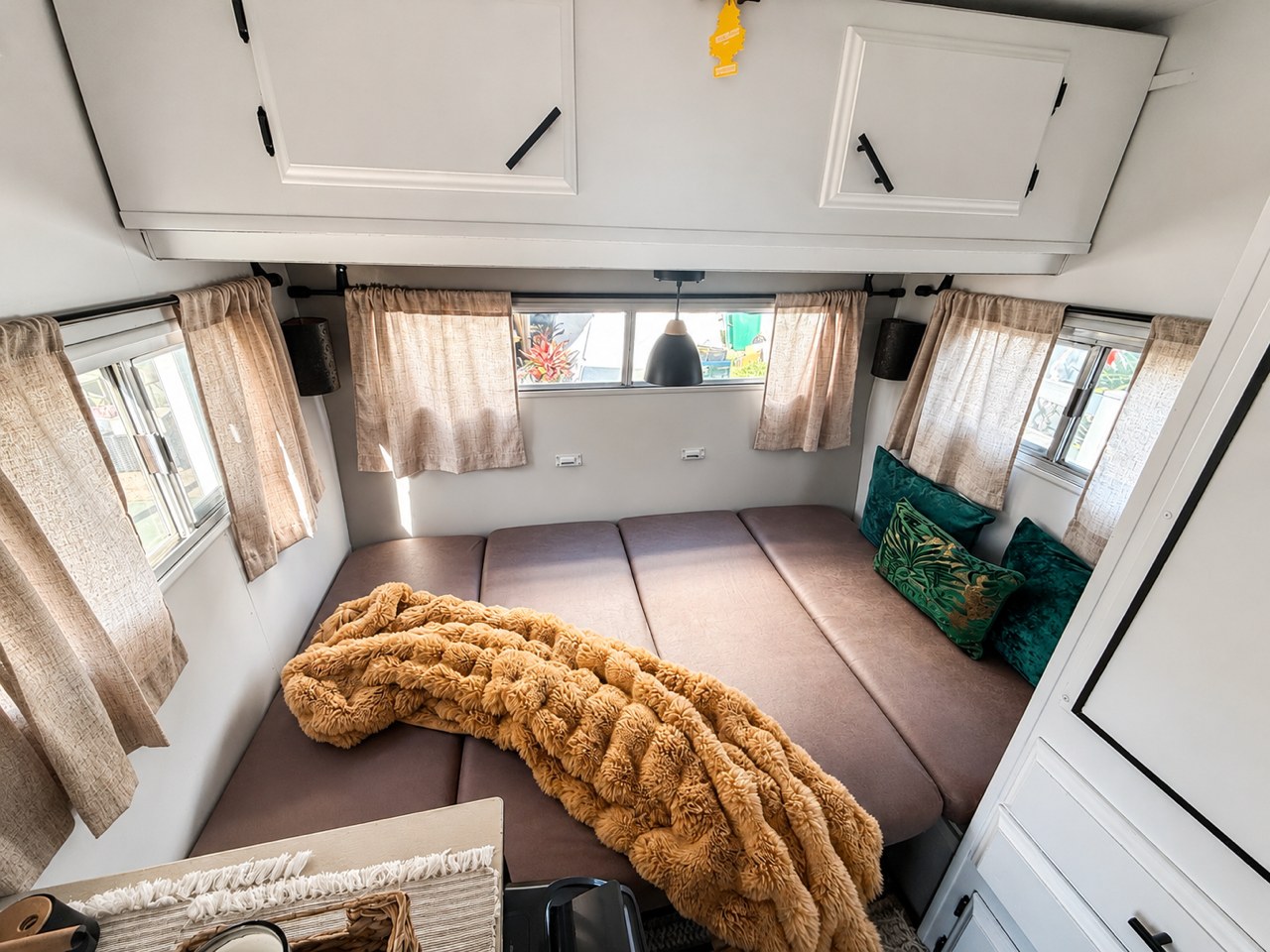 Relax in this charming RV rental featuring a plush bed with a soft orange blanket, green pillows, and bright windows.. Bell Coaches Bell 1300 1977
