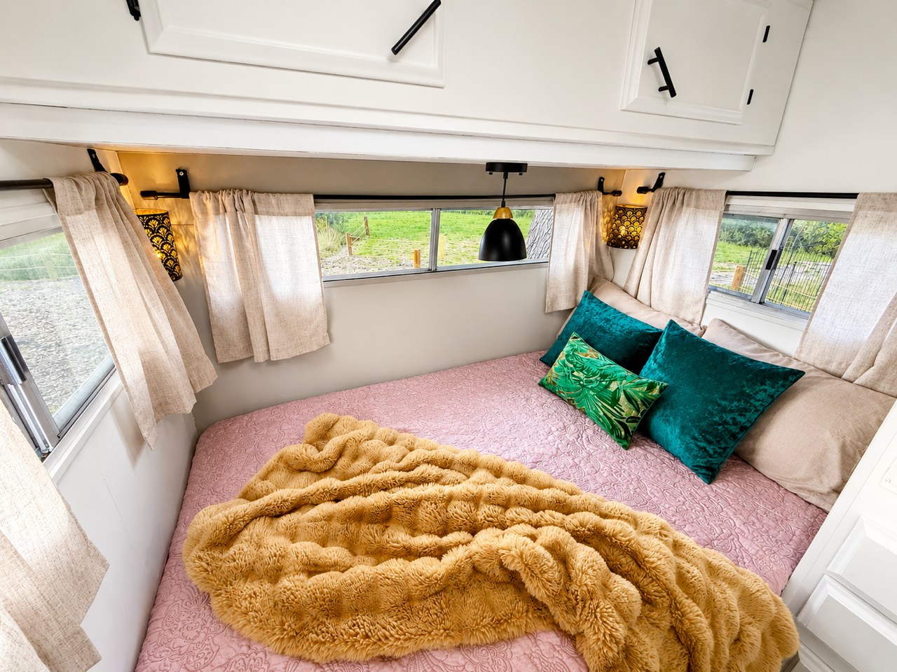 Cozy RV rental bedroom with a pink quilted bed, fuzzy orange blanket, and teal pillows, offering a comfortable stay.. Bell Coaches Bell 1300 1977