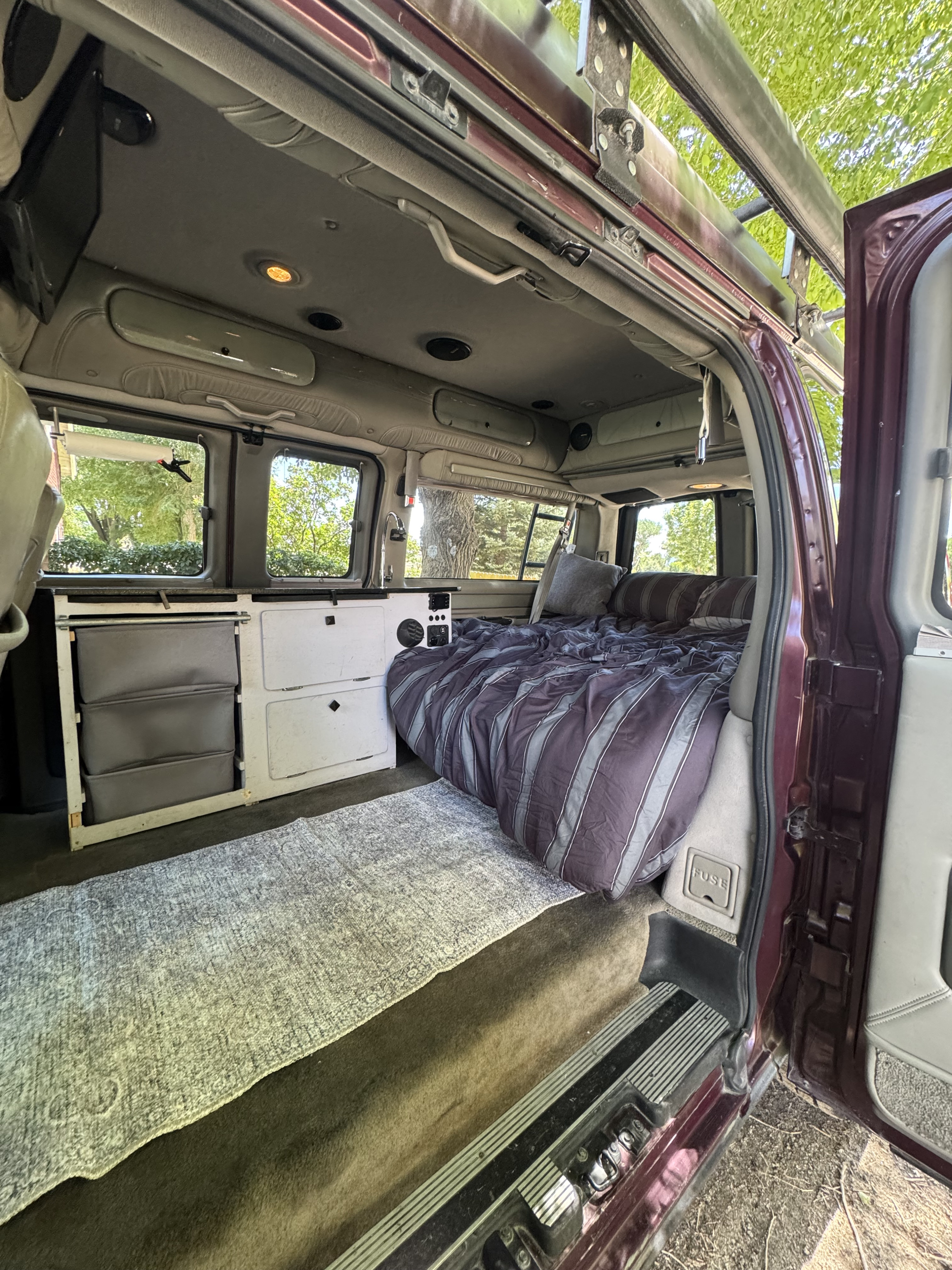 View inside an RV rental van's living area: striped bed, counter with sink, storage, and a floor rug.. Chevrolet Open Road 2005