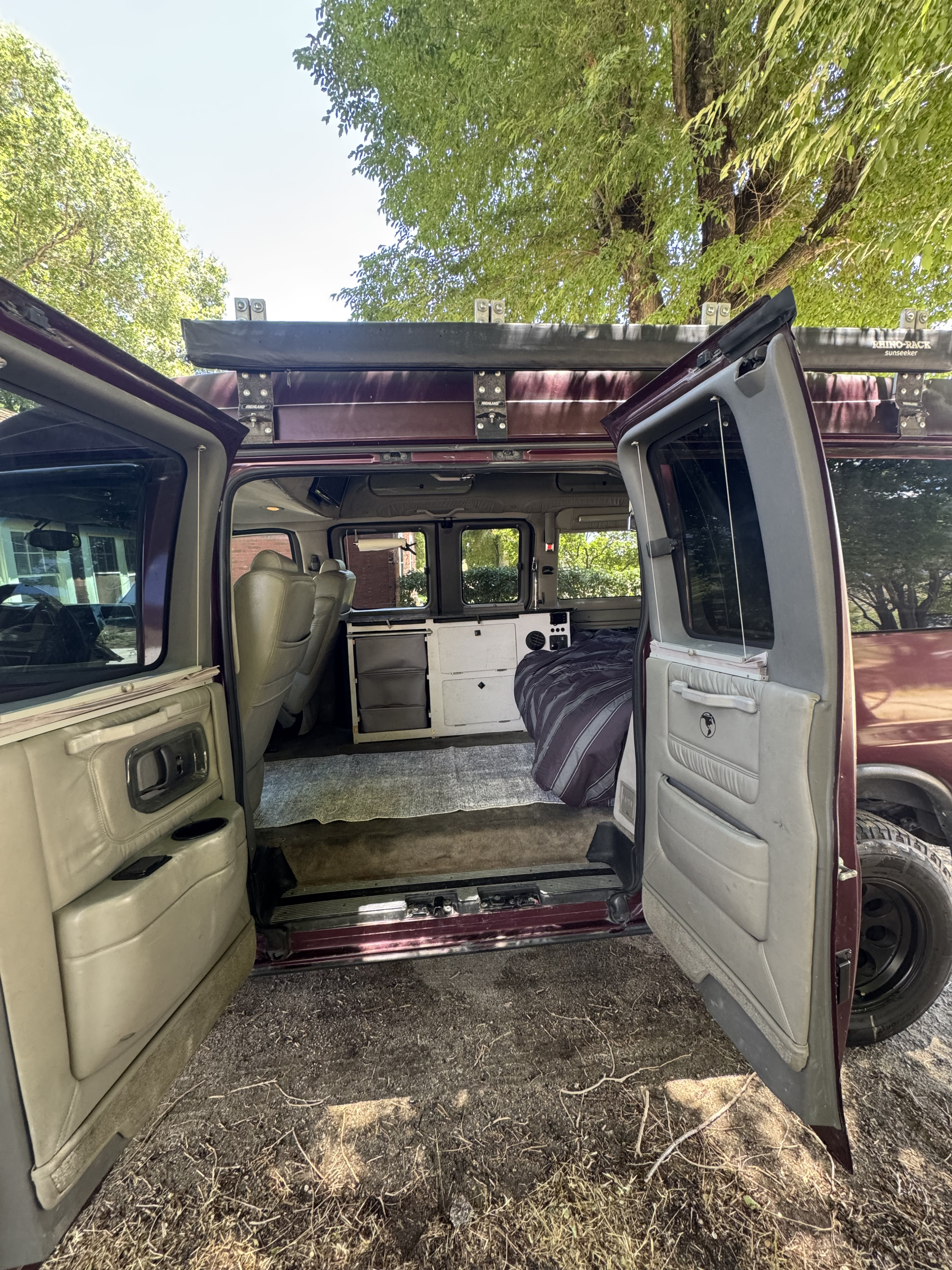 Converted camper van interior with doors open, showing bed & storage. Ideal for an RV rental outdoor adventure under green trees.. Chevrolet Open Road 2005