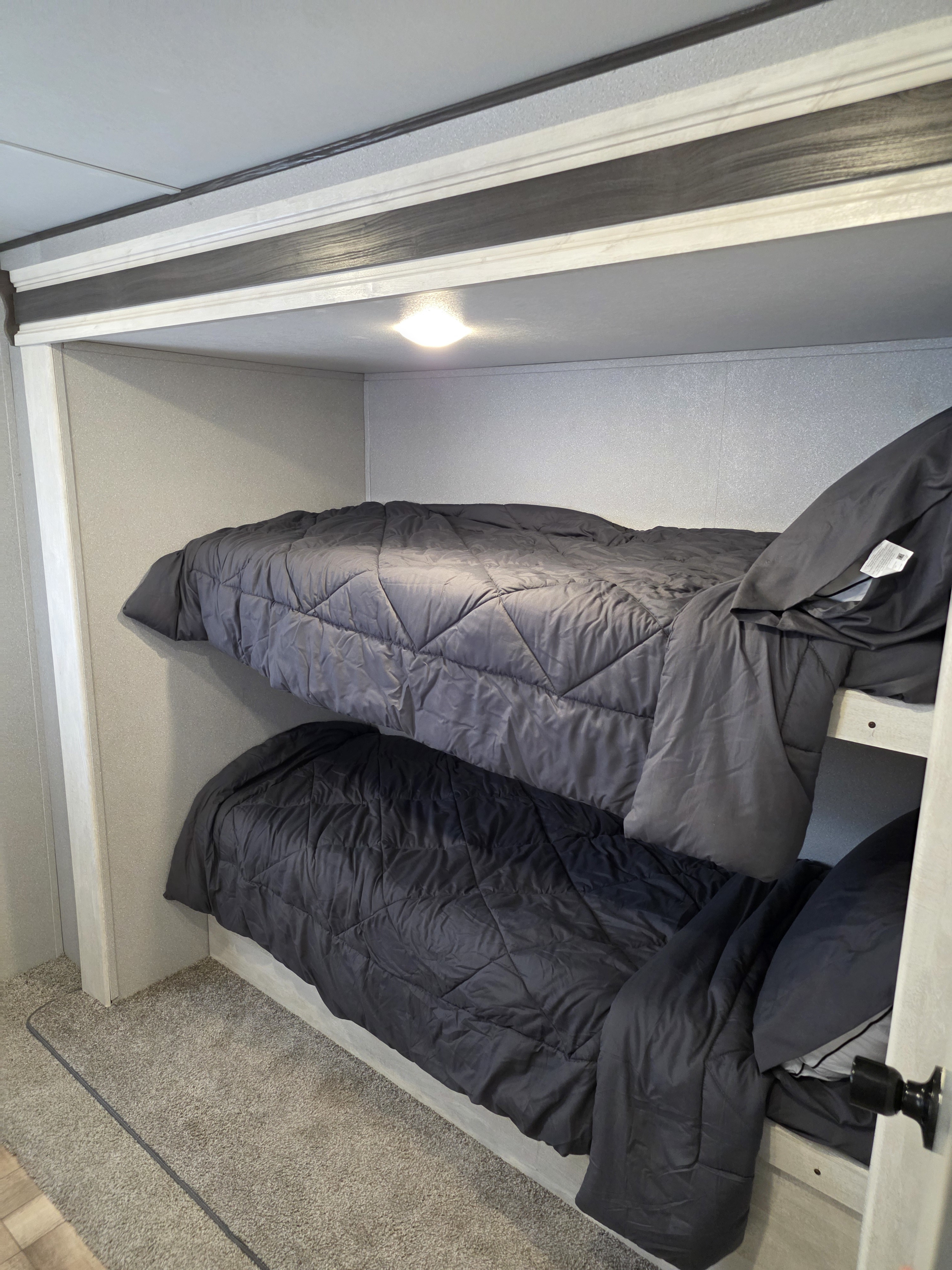 Interior of an RV rental with bunk beds, dark comforters, and an overhead light. Carpeted floor provides comfort for guests.. Shasta 32DS 2023