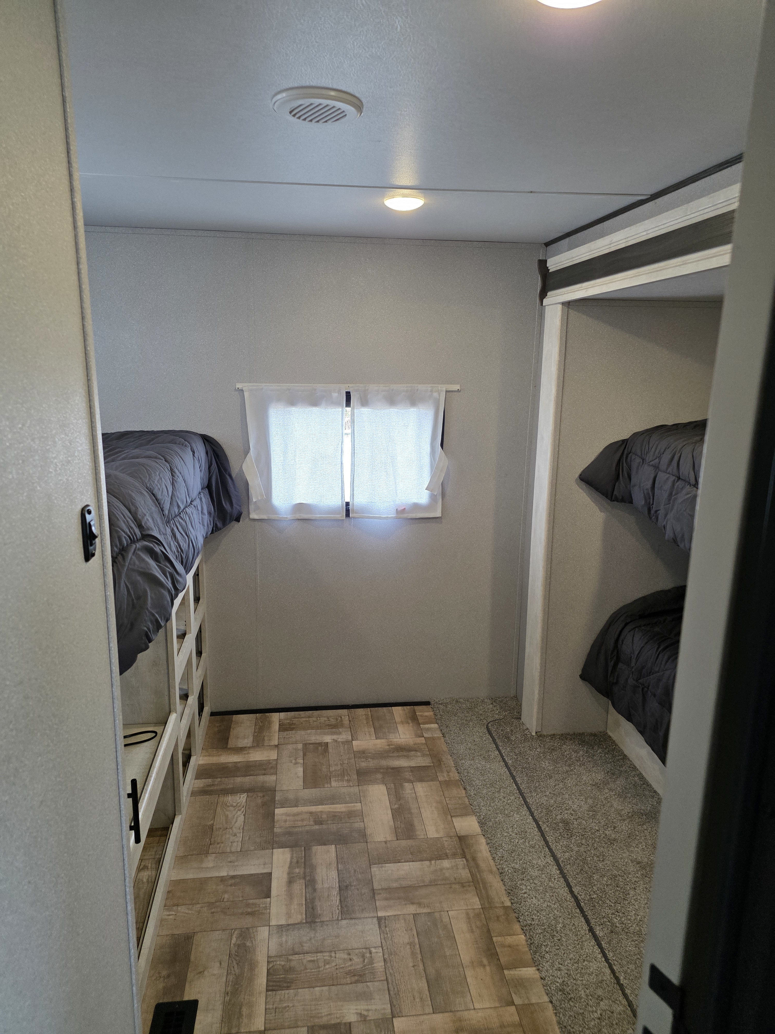 RV rental bunk room featuring dual bunk beds with gray comforters, wood-look floor, carpet, and a window with white curtains.. Shasta 32DS 2023