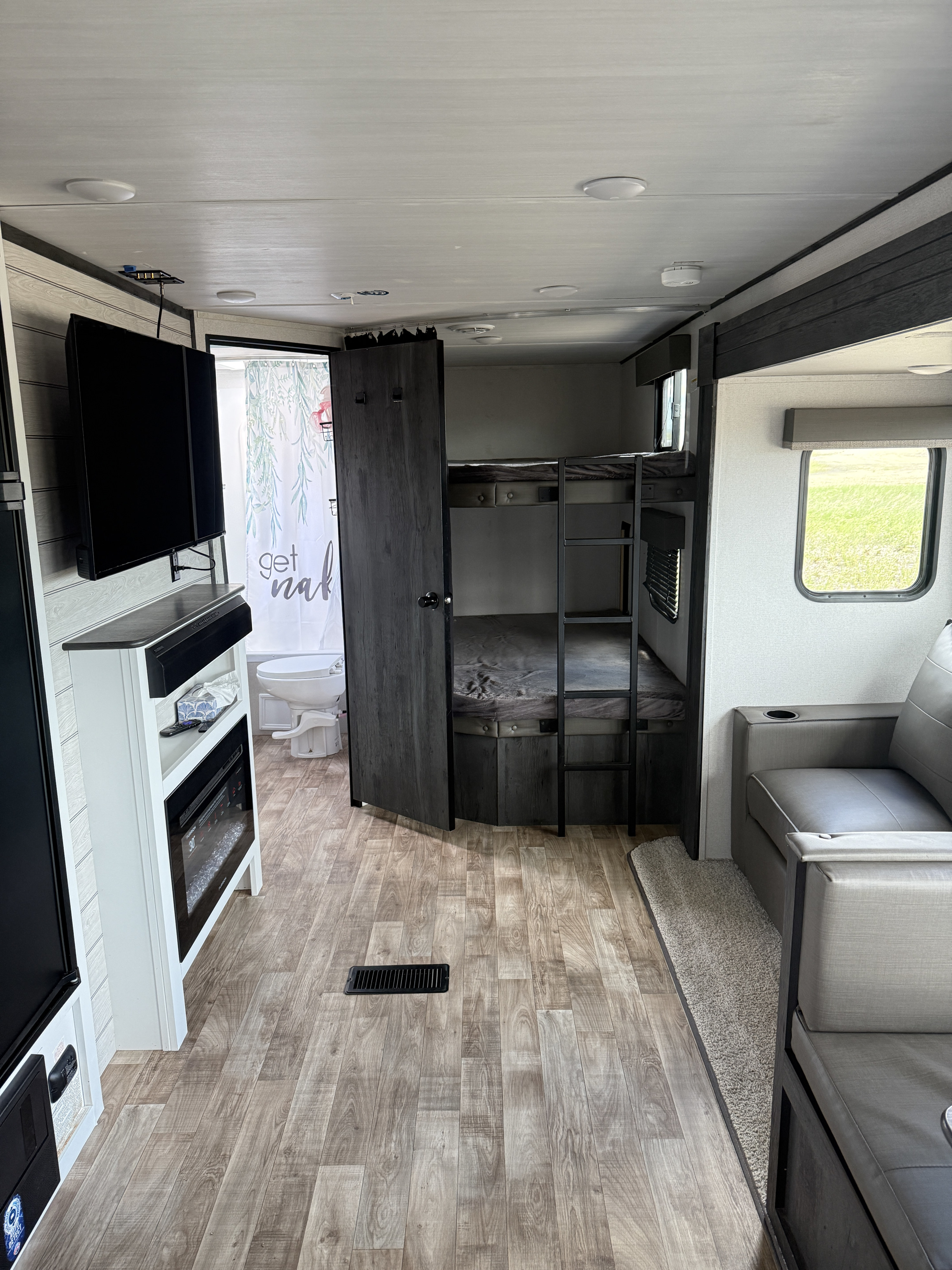 Step inside this RV rental, showcasing bunk beds, a sofa, TV, and a bathroom. A cozy camper interior with wood-look floors.. Keystone RV Hideout 2023
