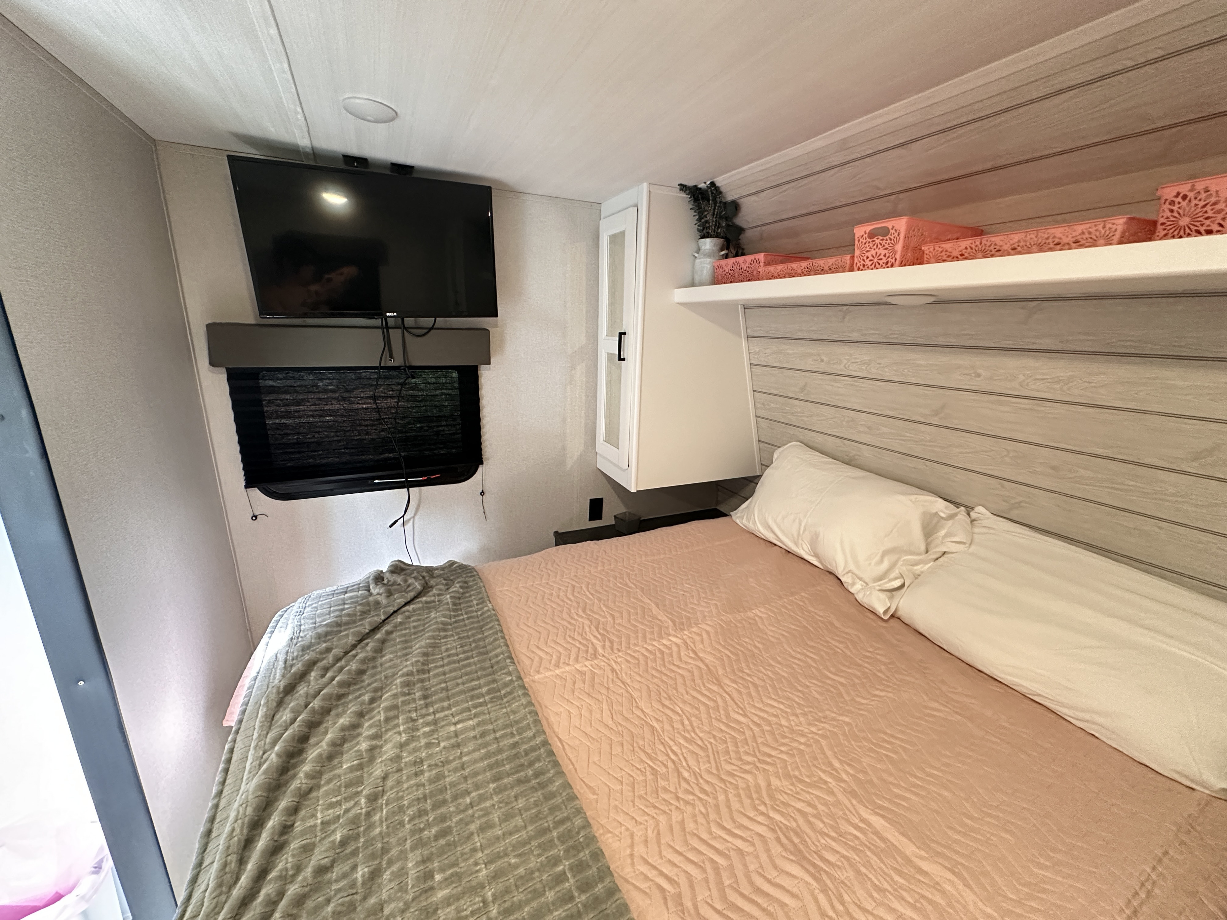 This RV rental's bedroom offers a cozy bed, wall-mounted TV, and functional overhead storage with pink accents.. Keystone RV Hideout 2023