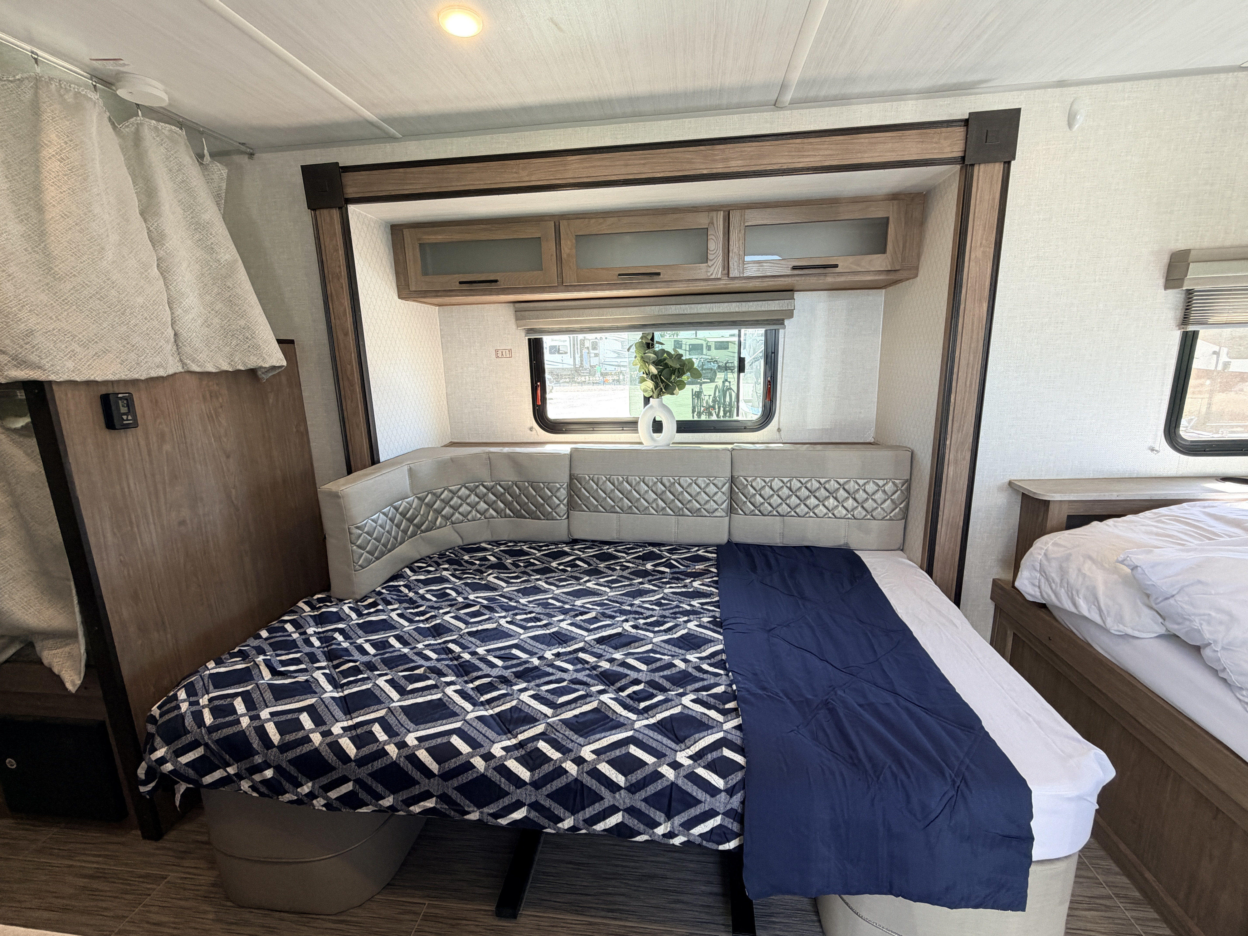RV rental bedroom with two cozy beds, overhead storage, a window, and patterned bedding.. No Boundaries 19 2021