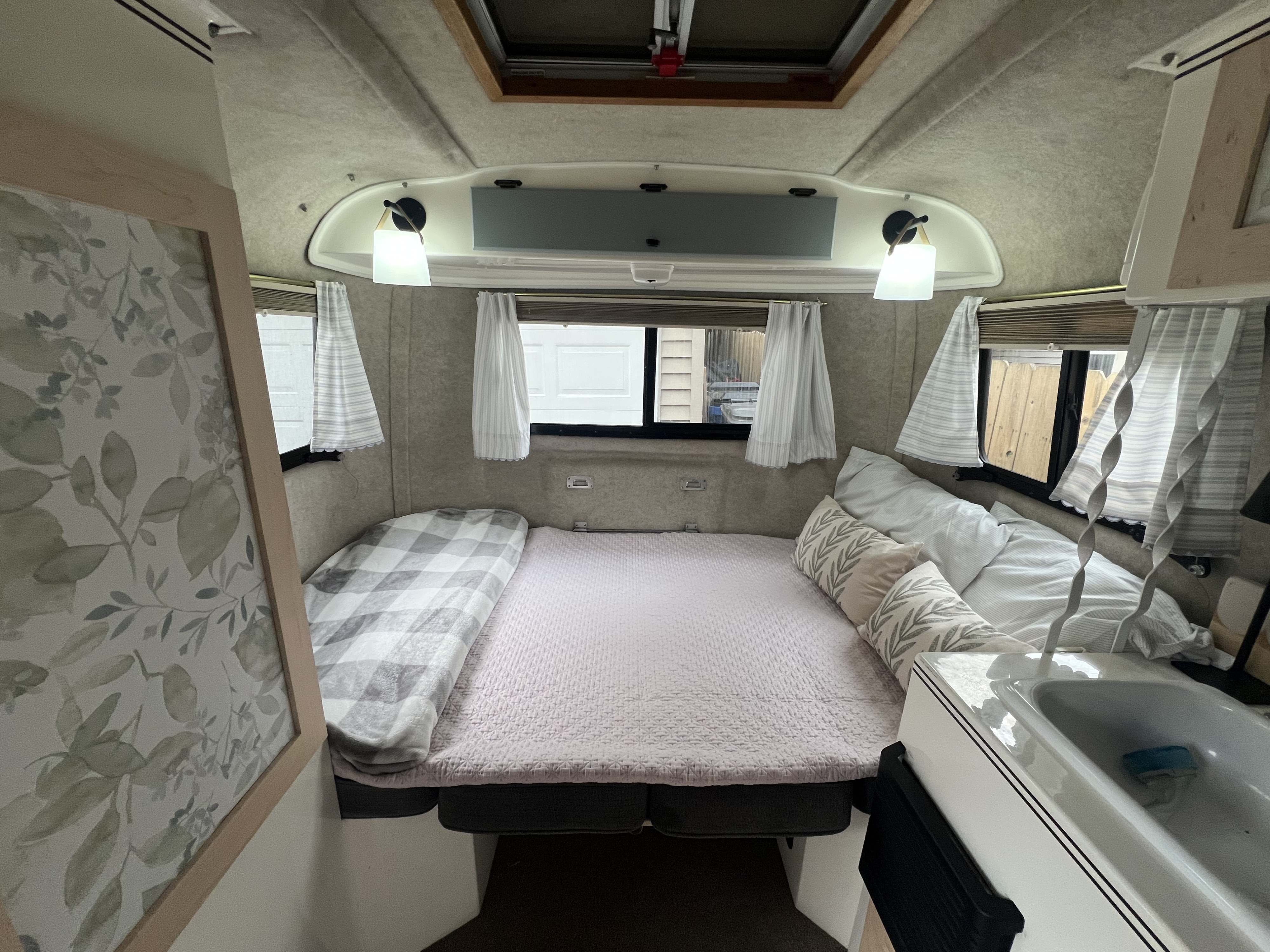 Explore this comfy RV rental bedroom area. Features a bed, leaf-patterned pillows, windows, and a compact sink.. Scamp Scamp Trailer 2011