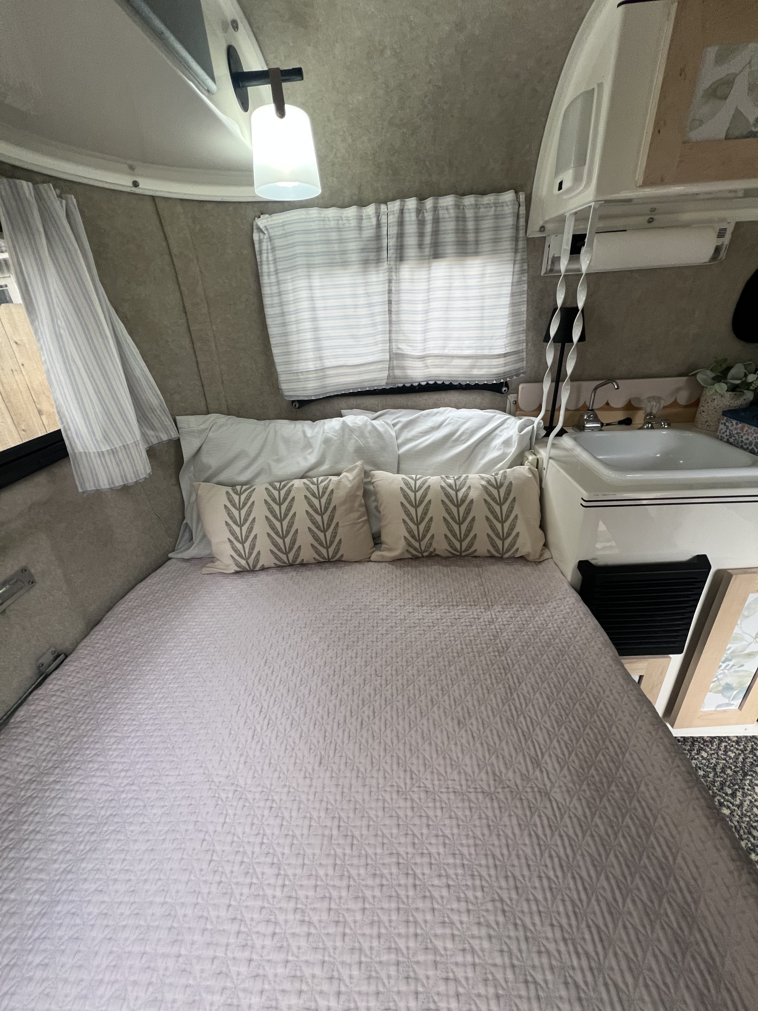 Bright RV rental interior showing a comfortable bed with neutral bedding, patterned pillows, and a small sink.. Scamp Scamp Trailer 2011