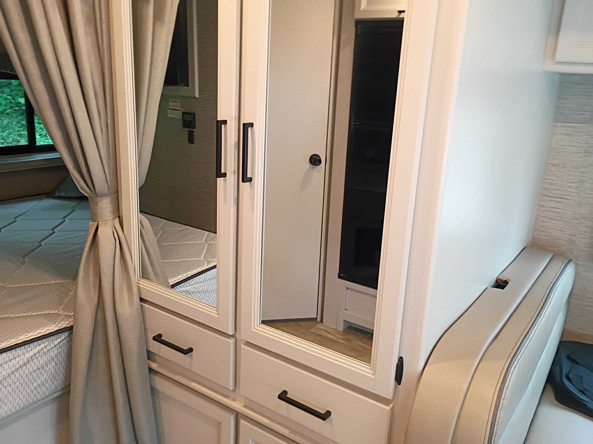 Inside an RV rental, a cozy bedroom area features a bed, mirrored wardrobe, and comfortable seating.. Thor Chateau 2023