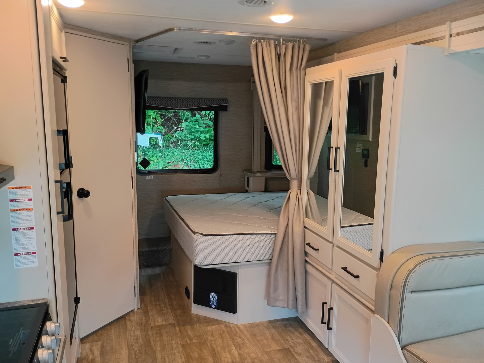 RV rental interior: a compact bedroom with a bed, TV, mirrored cabinets, and a nearby dining area.. Thor Chateau 2023