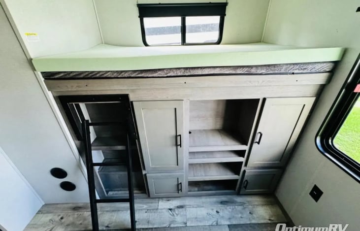 This rv rental features a bunk bed setup with a black ladder on the left, cabinetry and open shelves below, and a window above the top bunk.. Keystone RV Outback 2021