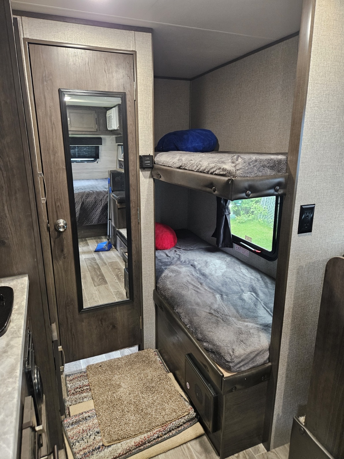 Inside this cozy RV rental, bunk beds offer sleeping space, with a window showing greenery. A full-length mirror reflects a bedroom view.. Jayco Jay Flight SLX 2021
