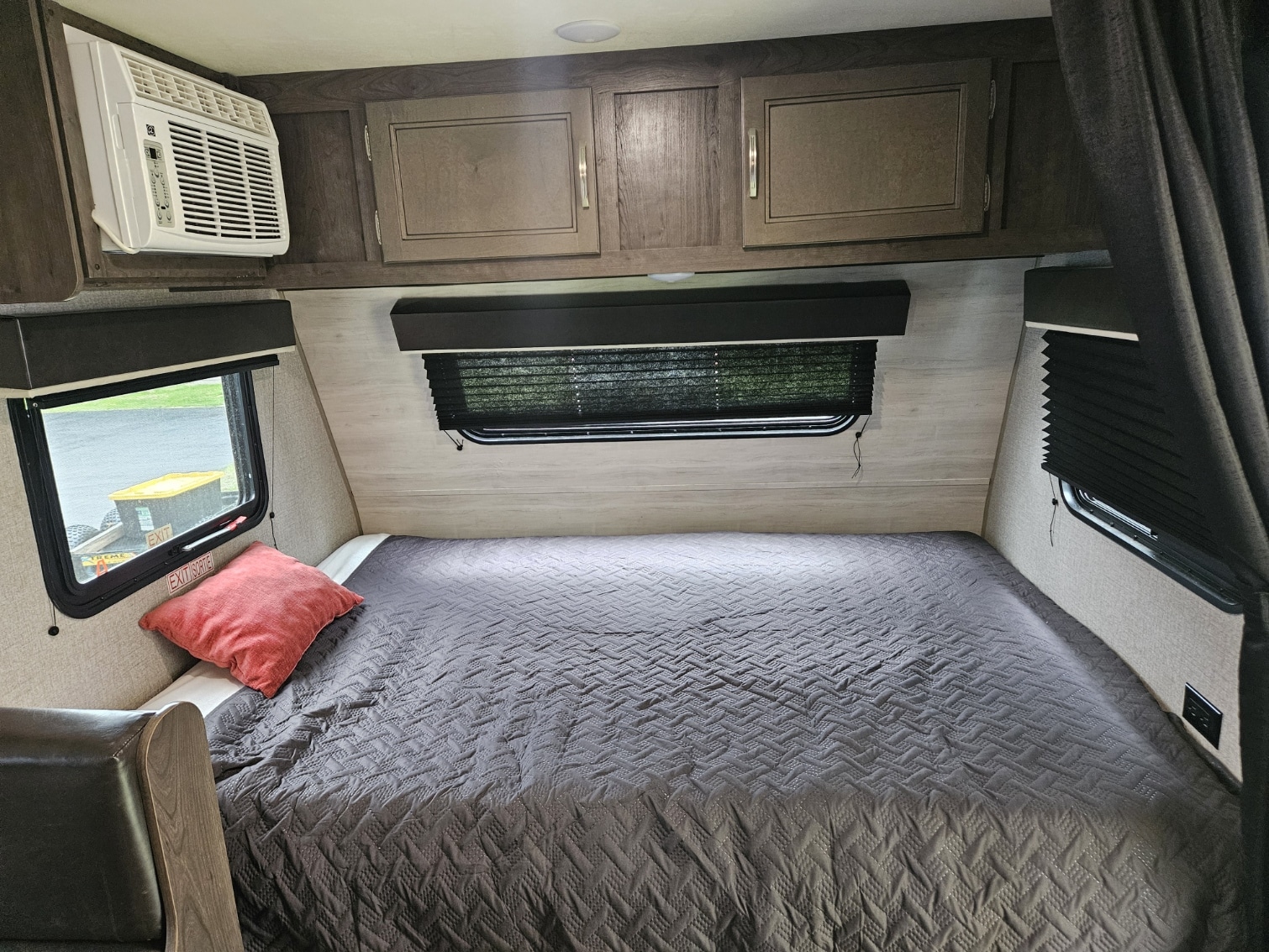 This comfortable RV rental bedroom has a gray quilted bed, window blinds, an AC unit, and overhead storage.. Jayco Jay Flight SLX 2021
