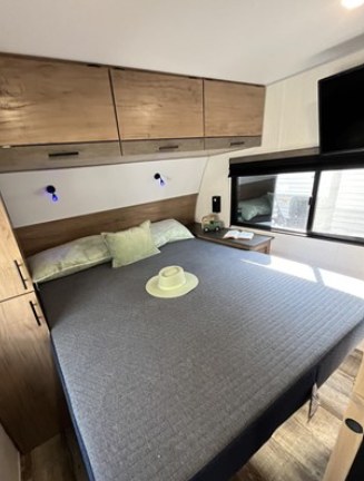Cozy RV rental bedroom with a comfortable bed, overhead cabinets, and a window for scenic views.. Forest River Campsite Reserve 23LM 2025