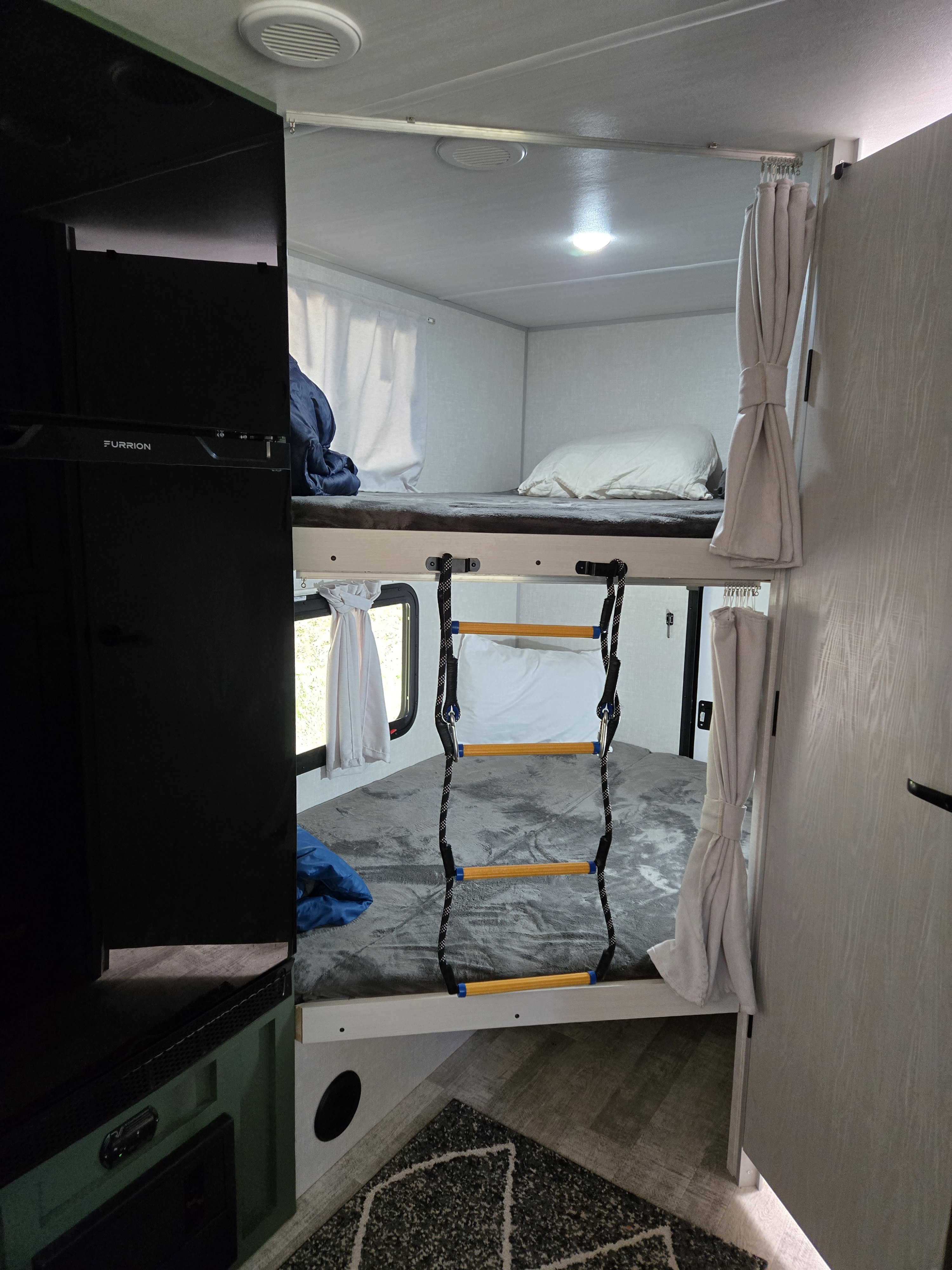 RV rental interior: stacked bunk beds with ladder, pillows, blankets, a window, and a black Furrion refrigerator on the left.. No Boundaries 20 2025