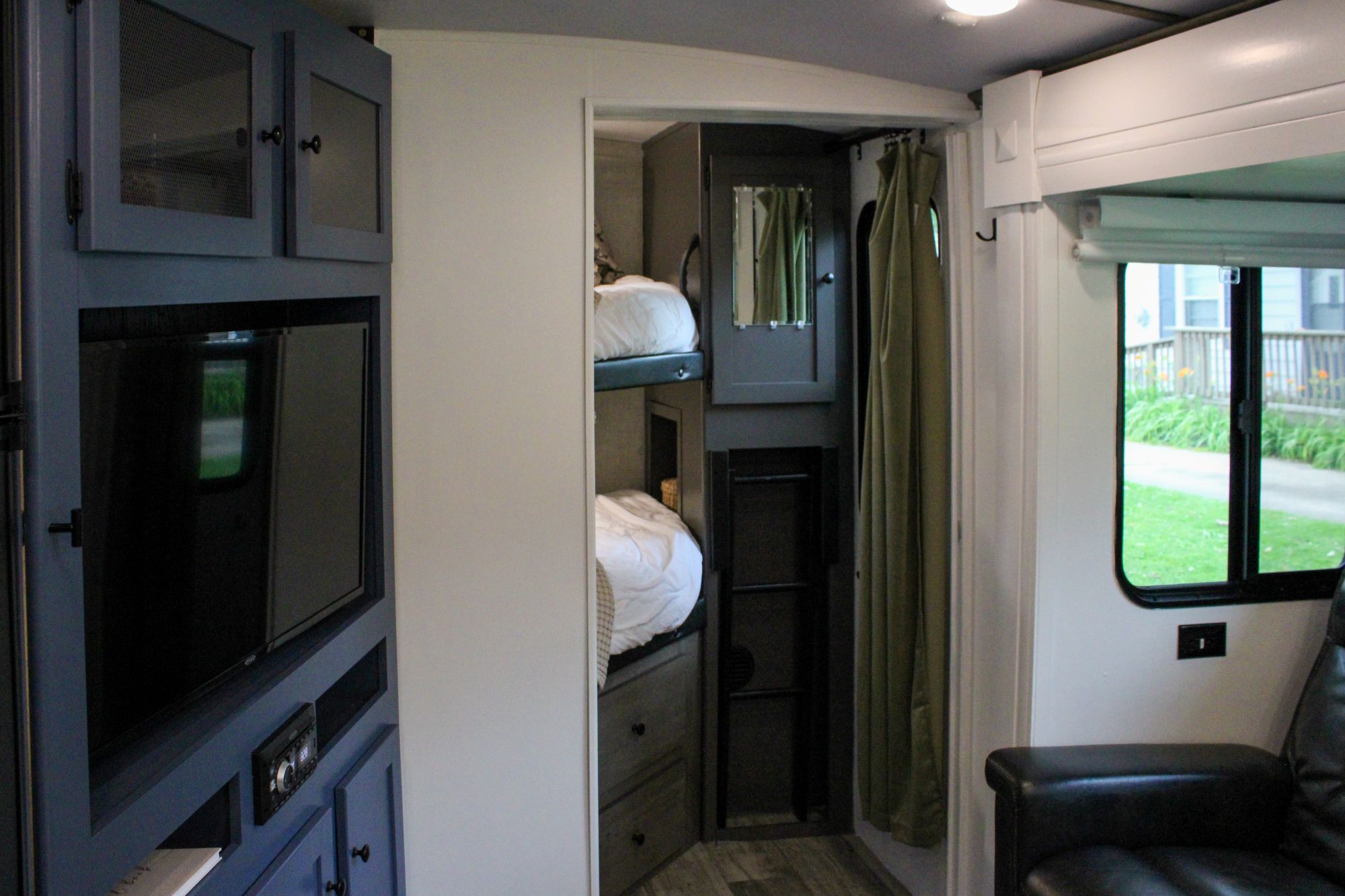 Cozy RV rental interior with blue cabinetry, TV, bunk beds, and a window offering a lush outdoor view.. Keystone RV Outback Ultra-Lite 2021