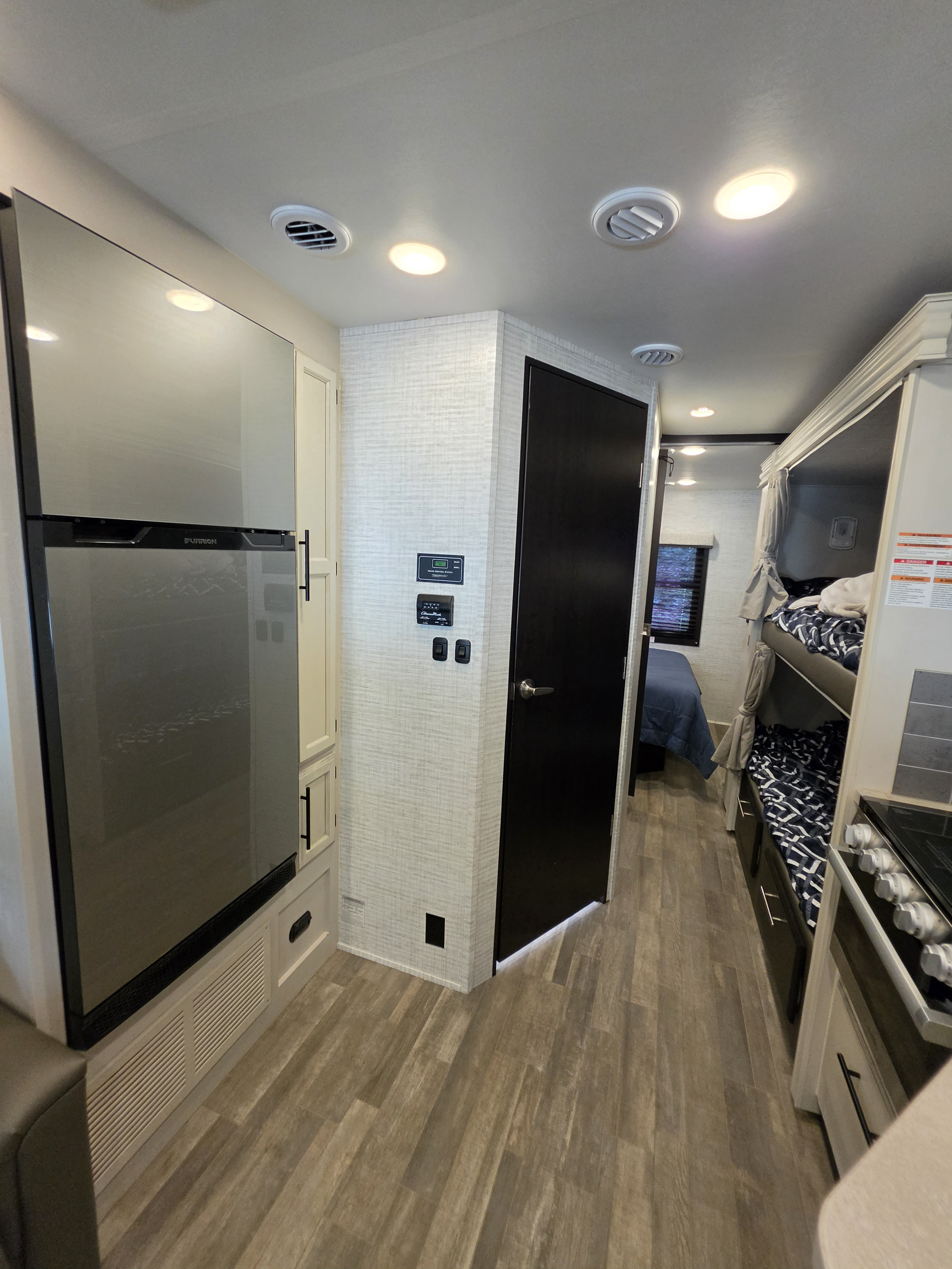 Bright RV rental interior: view of kitchen fridge, control panel, hallway leading to bunk beds & a private bedroom.. Jayco Redhawk 2024