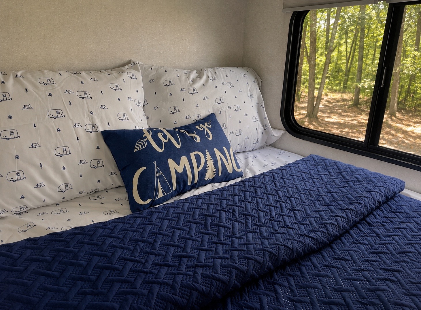 Cozy RV rental bedroom with camping-themed bedding, featuring a "Let's go CAMPING" pillow and a scenic forest view.. Forest River Cherokee Grey Wolf 2021