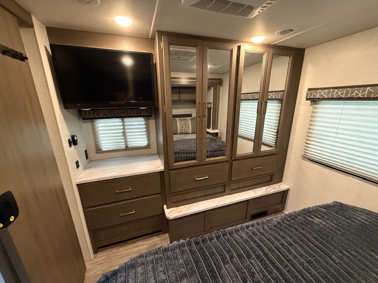 RV rental bedroom features a wall-mounted TV, mirrored wardrobe, dresser drawers, and a comfortable bed for guests.. Thor Resonate 2025