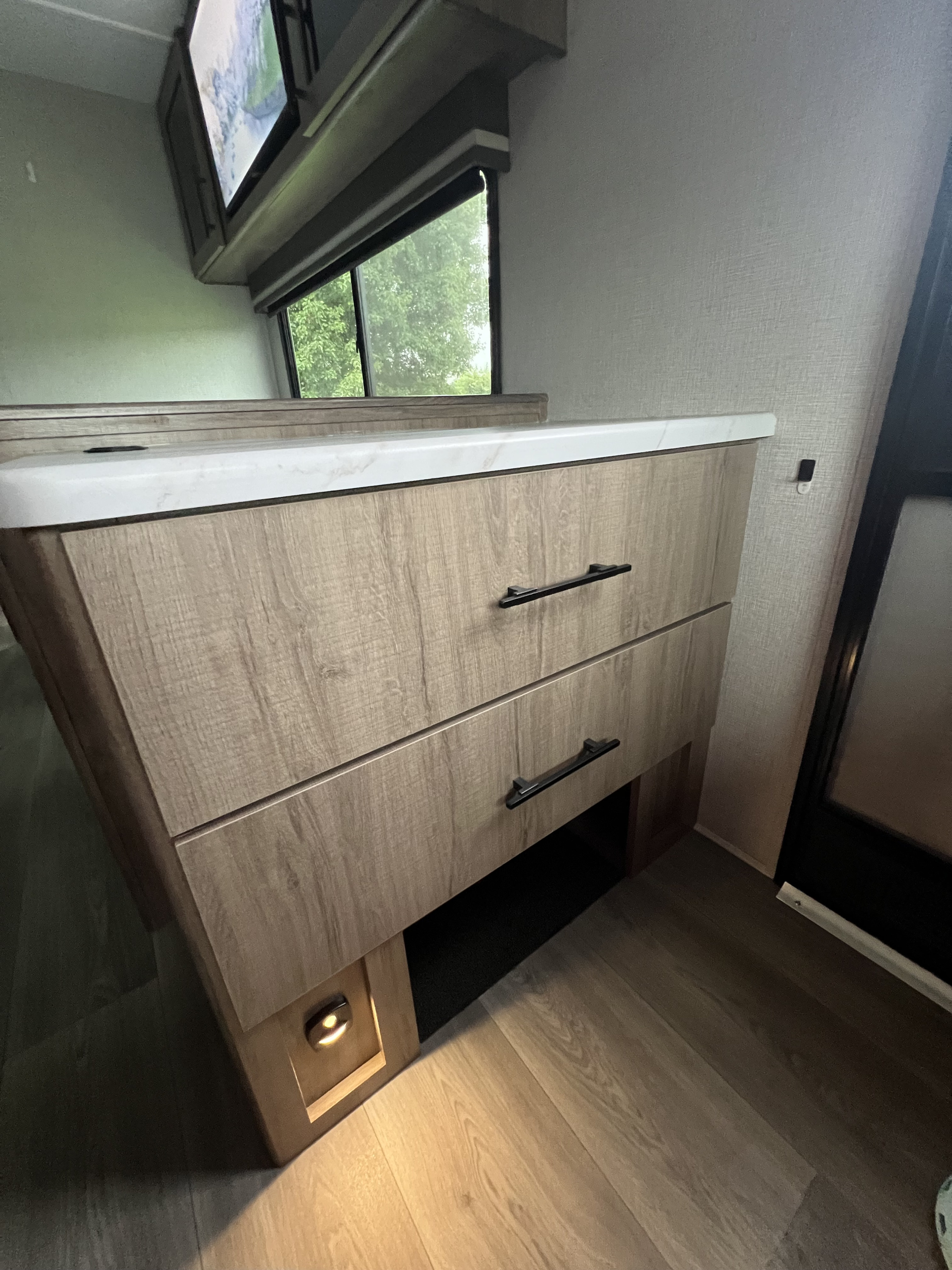 RV rental interior: wood-grain cabinet, two drawers with black handles, white countertop, and light wood flooring.. Grand Design Imagine XLS 2024