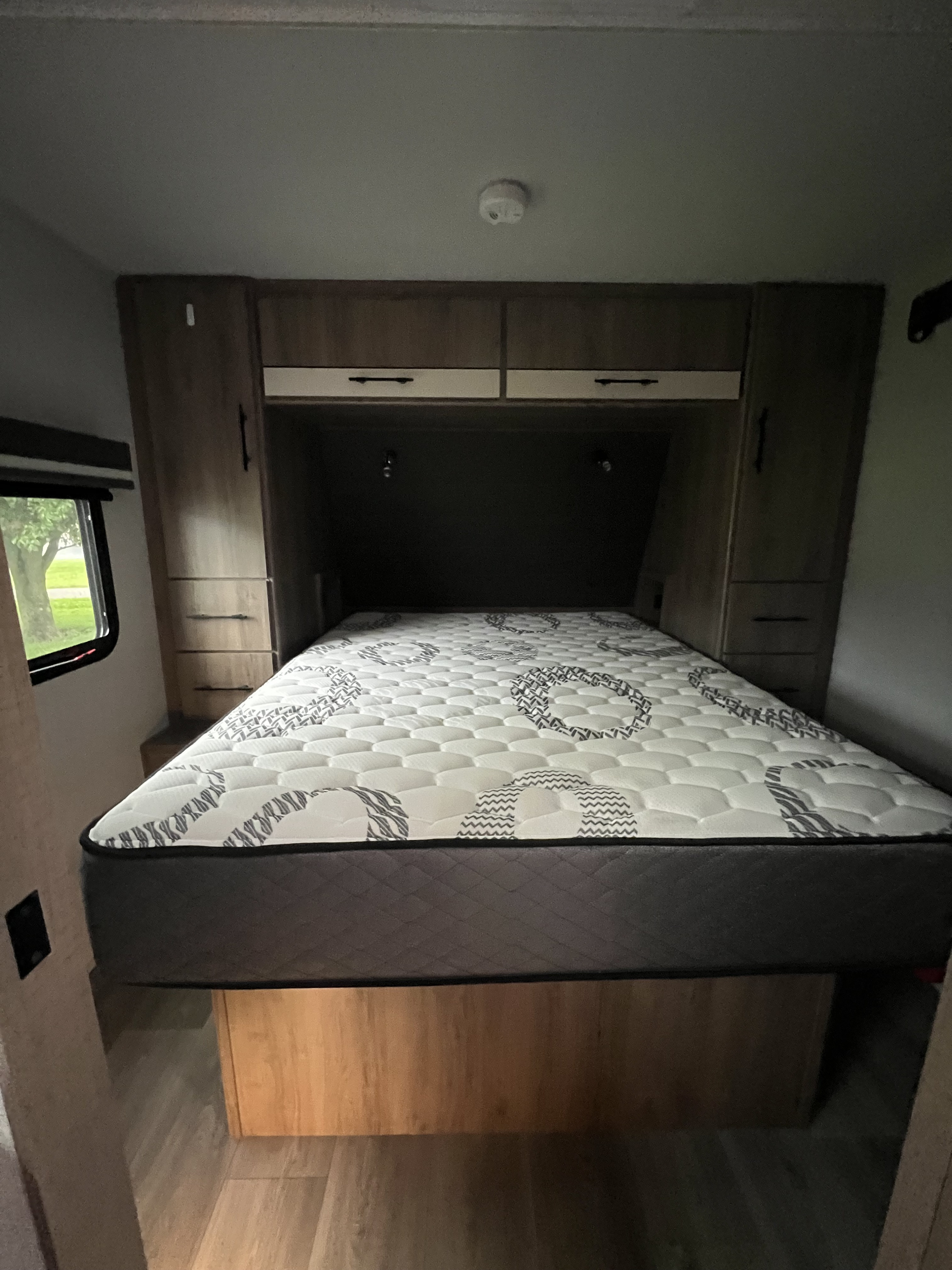 Cozy RV rental bedroom featuring a patterned mattress, built-in cabinets, and a window view for comfortable travel.. Grand Design Imagine XLS 2024