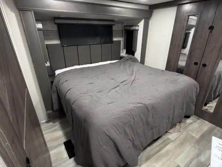 Comfortable RV rental bedroom featuring a large bed with grey bedding, modern headboard, overhead storage, and mirrored closets.. Alliance RV Paradigm 2021