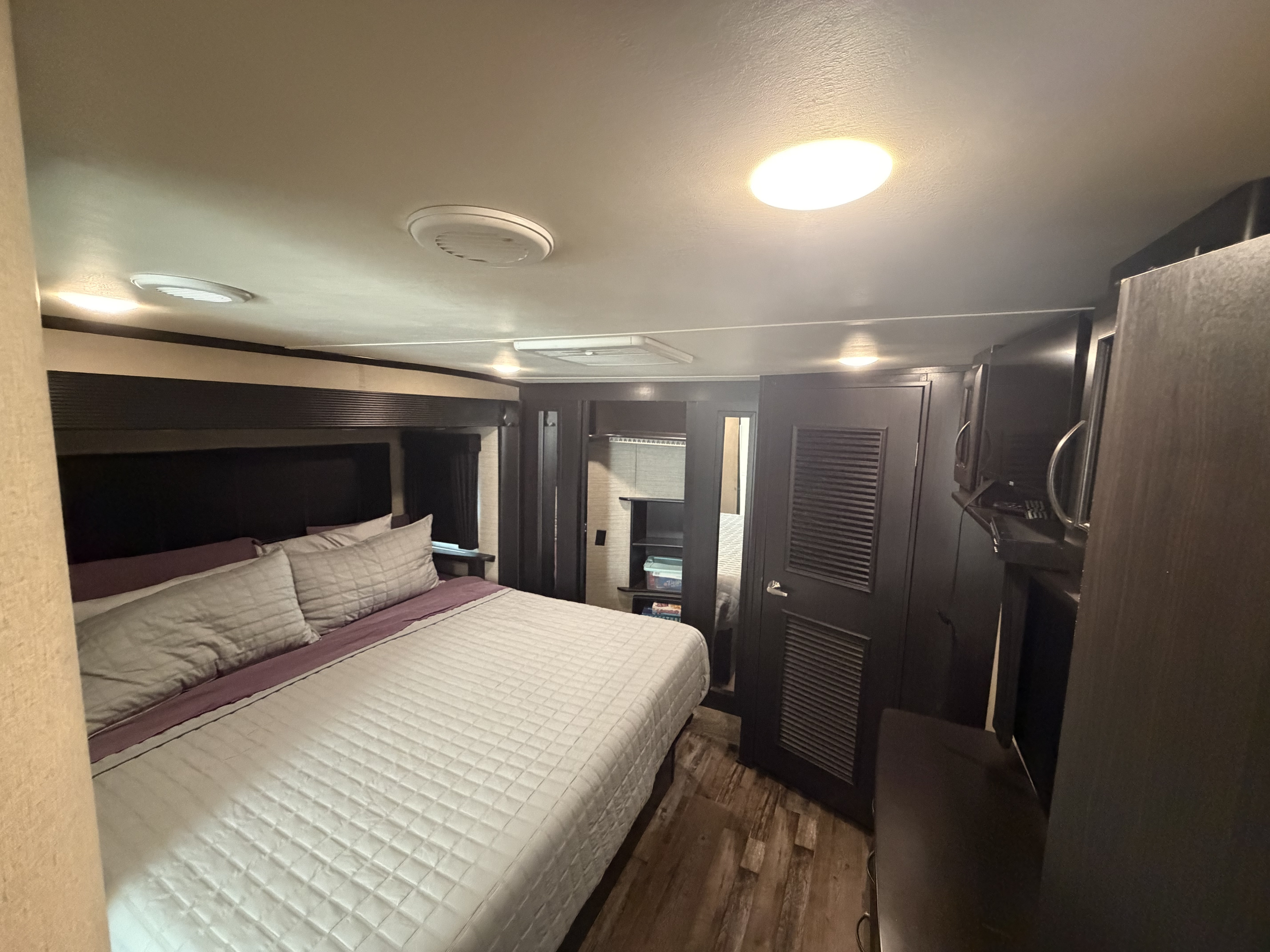 Cozy RV rental bedroom interior, featuring a comfortable bed with grey bedding, dark wood cabinets, and bright ceiling lights.. Denali Denali Fifth Wheel 2017