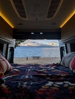 Wake up to amazing views! This RV rental offers a cozy bed looking out to a serene beach, calm lake, & distant mountains.. Mercedes Sprinter Motorhome Campervan RV 2025
